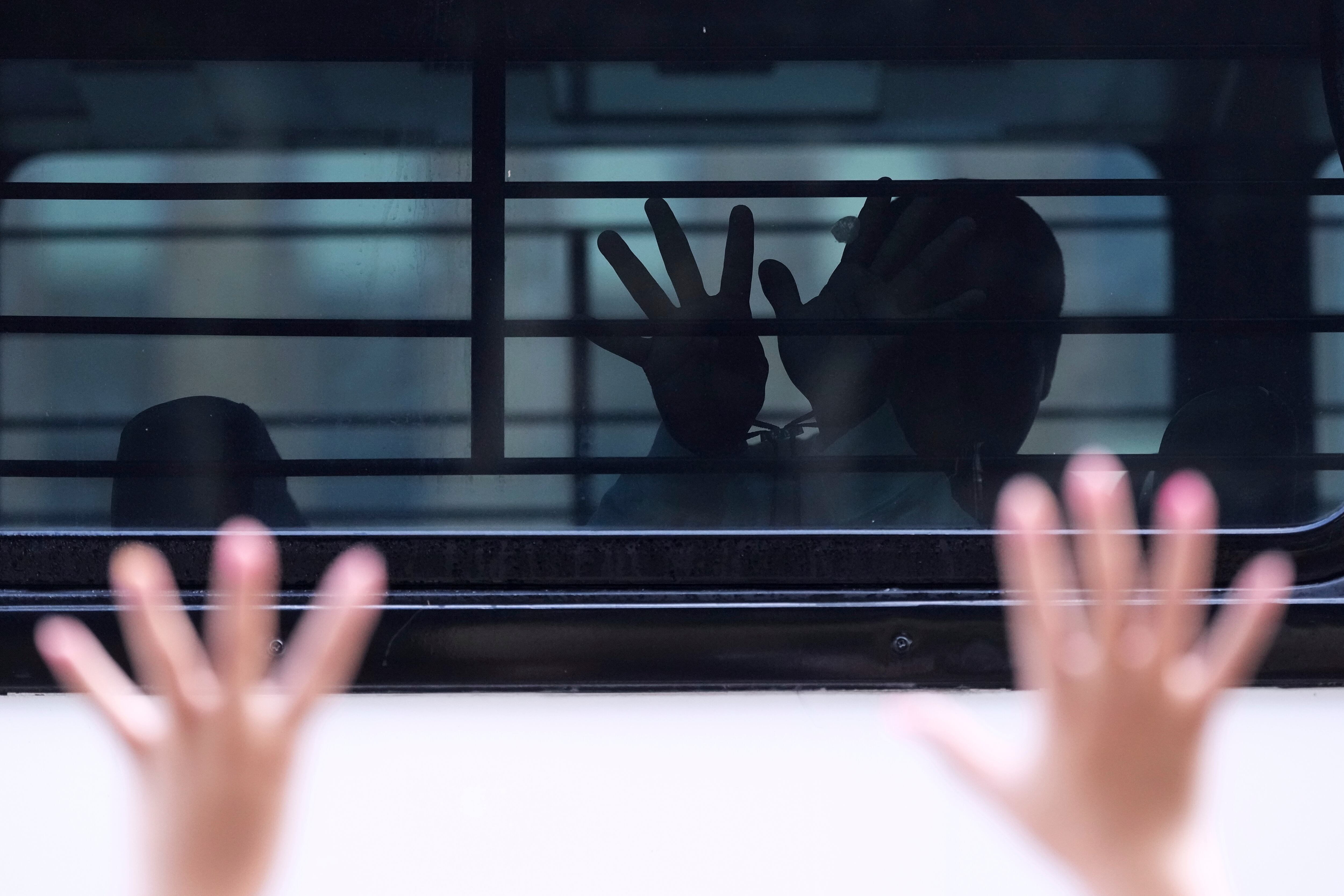 A man who was detained and placed on a bus by federal agents following an appearance at immigration court tries to communicate through barred and tinted windows, July 28, in San Antonio, Texas.