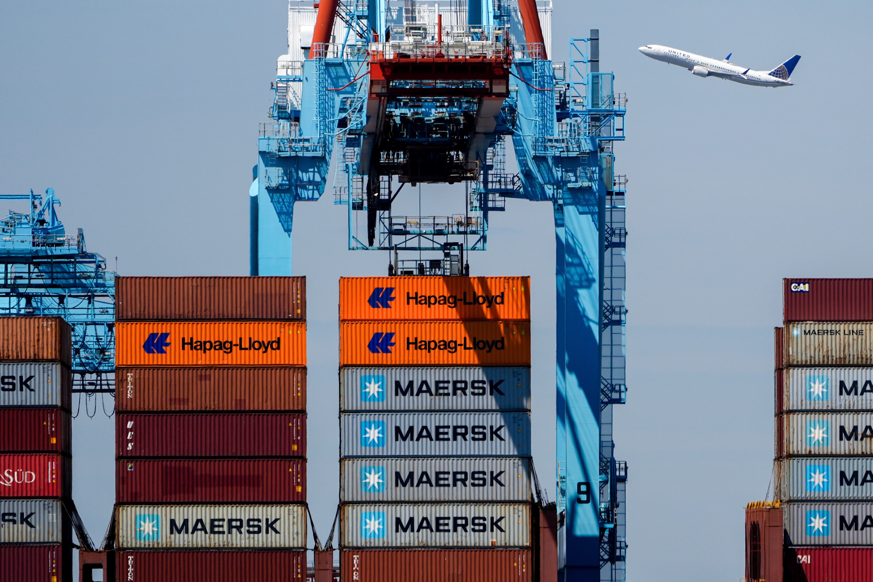 An airplane flies over the container ship Alexandra at the Port Newark Container Terminal, April 18, in Newark, N.J.