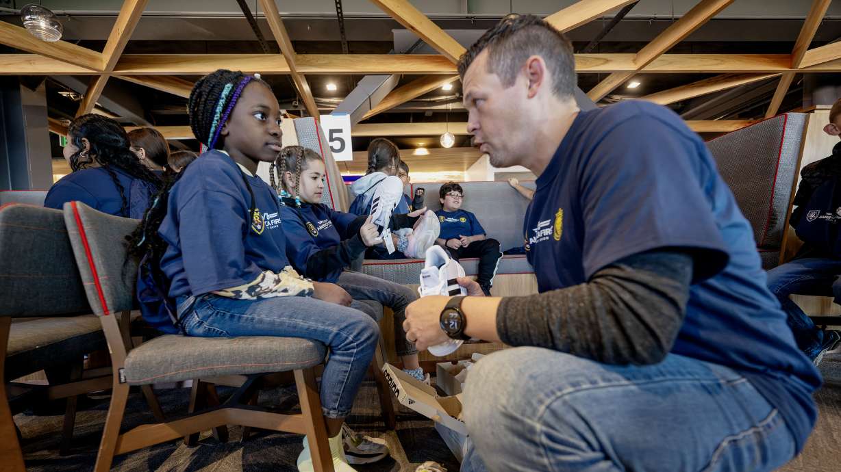 Brett Greenwell helps Schineha Aka put on new shoes as he and other America First employees join with Real Salt Lake as part of the 30th year of the credit union’s “Warm the Soles” tradition.