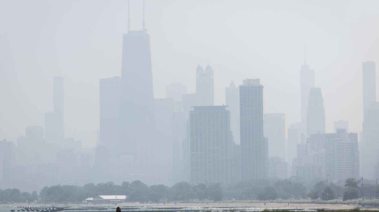 People sun tan in grass off the Lakefront Trail on the North Side as a haze of Canadian wildfire smoke blankets the Chicago area and creates poor air quality, Thursday.
