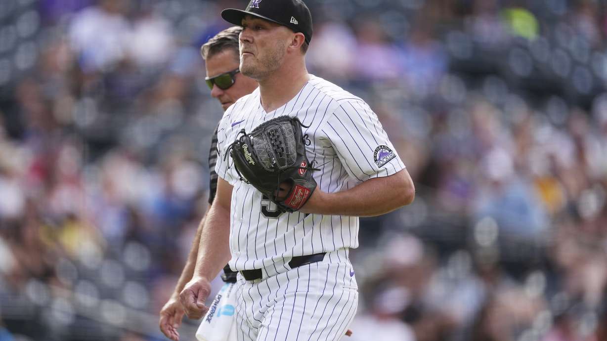 Colorado Rockies relief pitcher Seth Halvorsen, front, is escorted from the mound by head trainer Keith Dugger after throwing only five pitches to Pittsburgh Pirates pinch hitter Spencer Horwitz in the ninth inning of a baseball game Saturday, Aug. 2, 2025, in Denver.