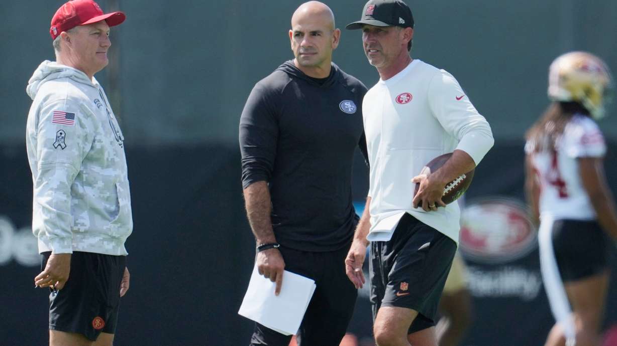 FILE - San Francisco 49ers general manager John Lynch, left, talks with defensive coordinator Robert Saleh, middle, and head coach Kyle Shanahan during practice at the team's NFL football training camp, Wednesday, July 23, 2025, in Santa Clara, Calif.