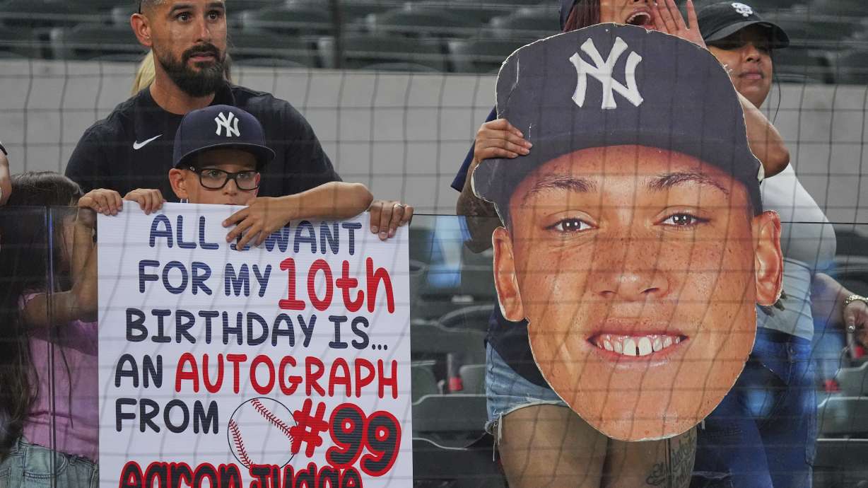 Fans in the stands hold signs before a baseball game between the New York Yankees and the Texas Rangers, Monday, Aug. 4, 2025, in Arlington, Texas.