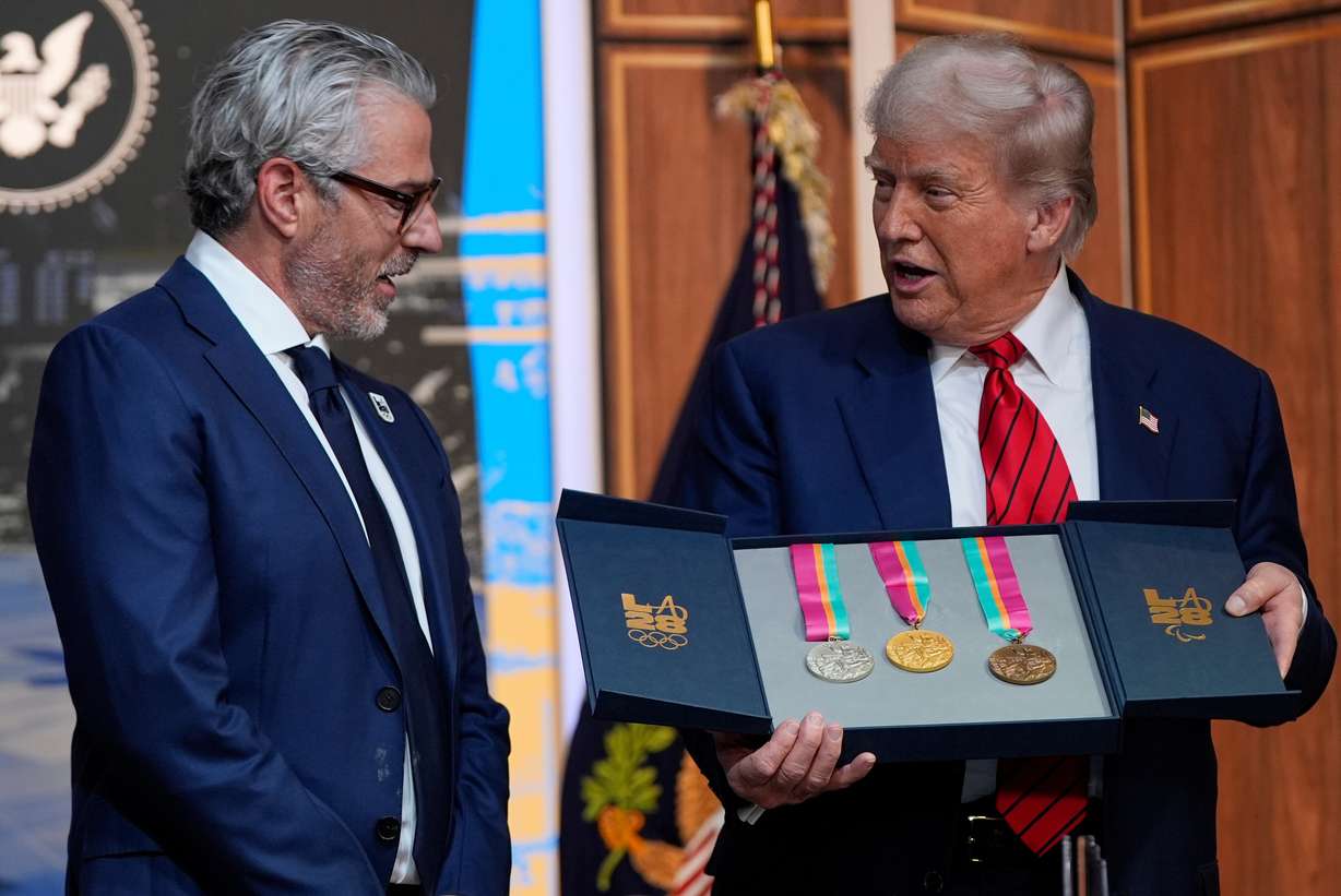 President Donald Trump listens as Casey Wasserman, chairman of LA28, presents him with a full set of medals from the 1984 Olympics in Los Angeles, during an event regarding the 2028 Los Angeles Olympic Games, in the South Court Auditorium of the Eisenhower Executive Office Building on the White House campus, Tuesday, in Washington.