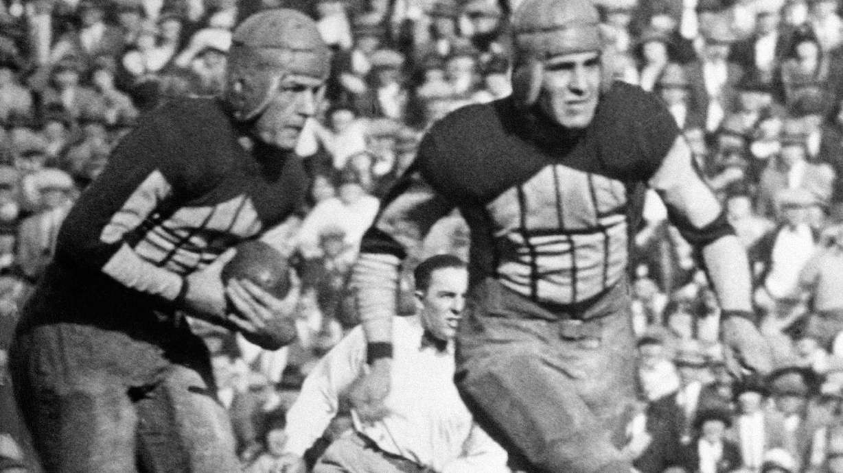 FILE - Illinois' Red Grange, left, follows a blocker on a 95-yard kickoff return for a touchdown against Michigan during a college football game on Oc.t 18, 1924, in Champaign, Ill.