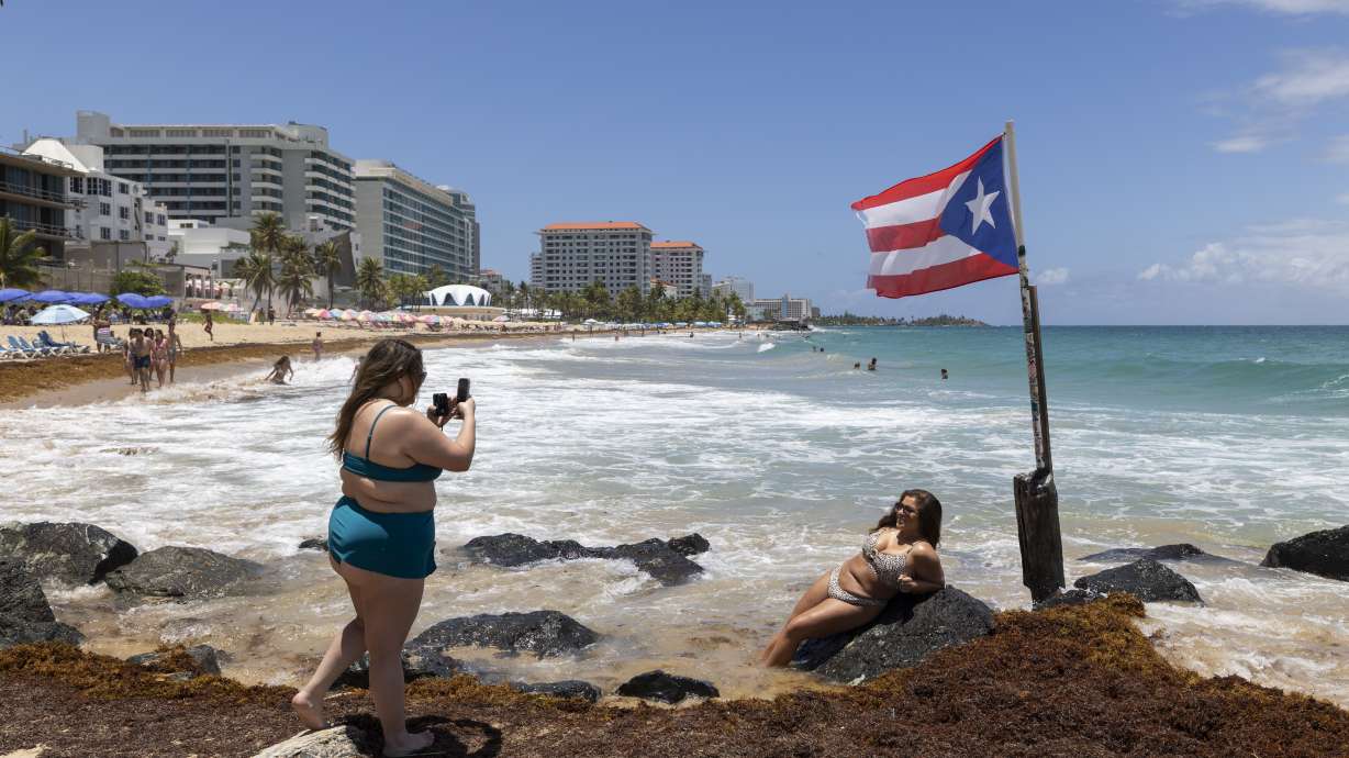 A woman poses for photos next to a Puerto Rican flag along the beach in Condado, Puerto Rico, as Hurricane Erin approaches, Friday. The storm was downgraded to a Category 3 hurricane on Sunday.