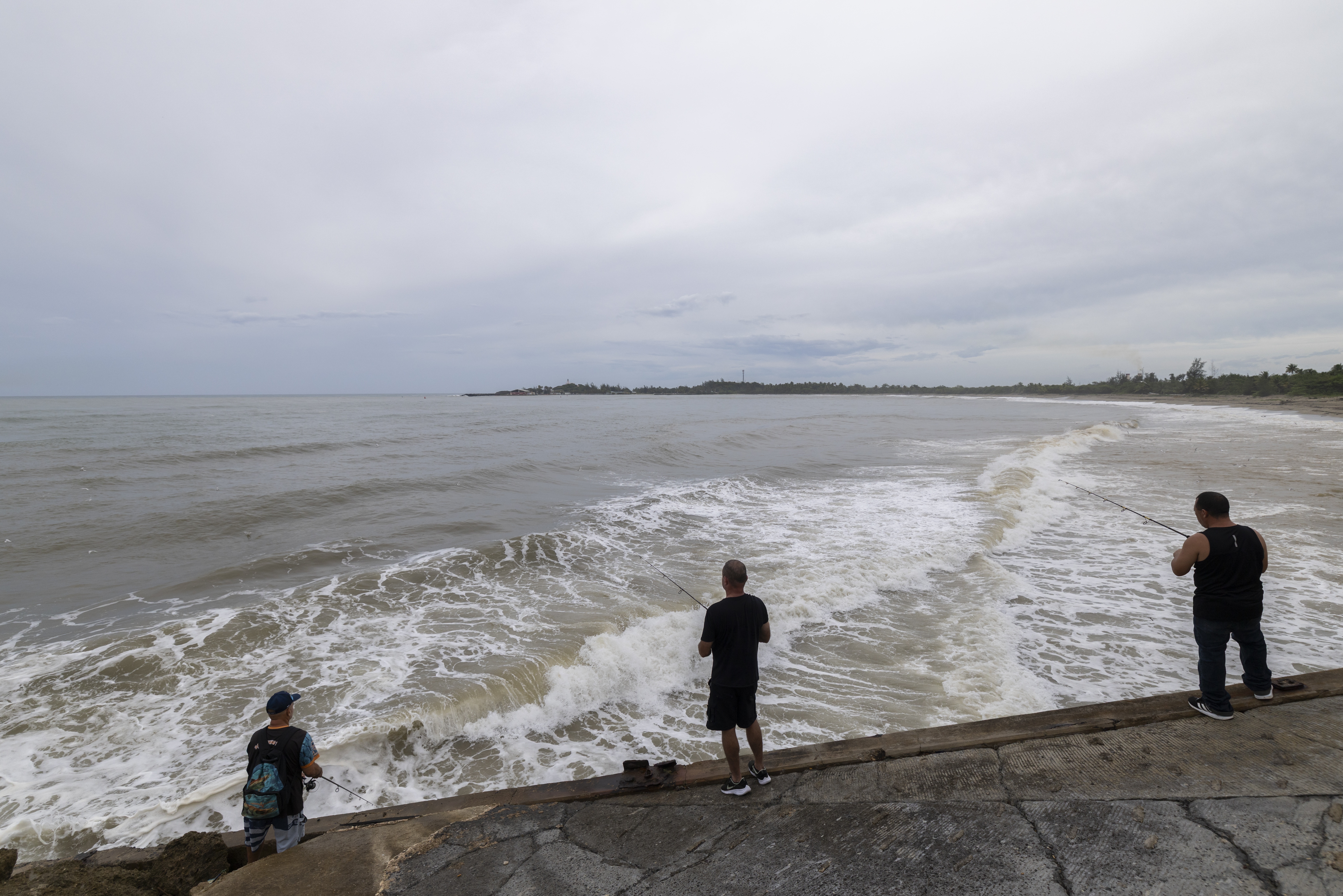 People fish along the shore in Arecibo, Puerto Rico, as Hurricane Erin brings rains to the island, Sunday.