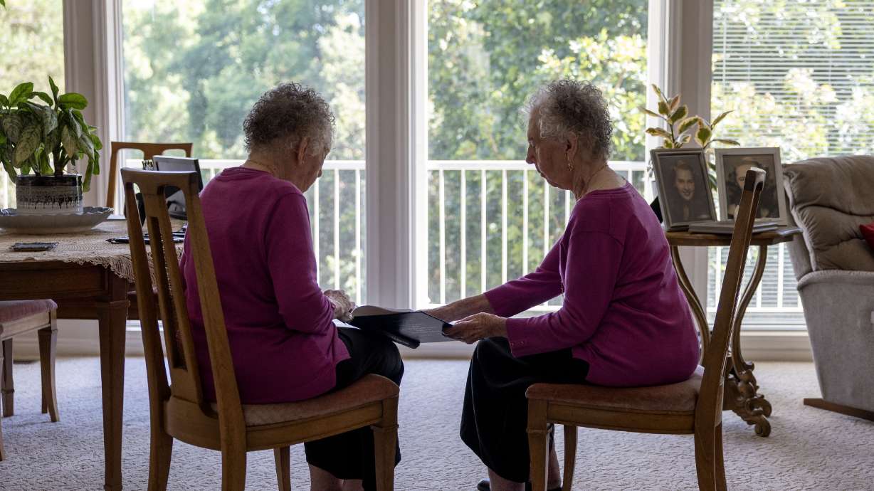 Twin sisters Verla Starkey, left, and Merla Swenson look at a book of their family history at their home in Kaysville on Wednesday.