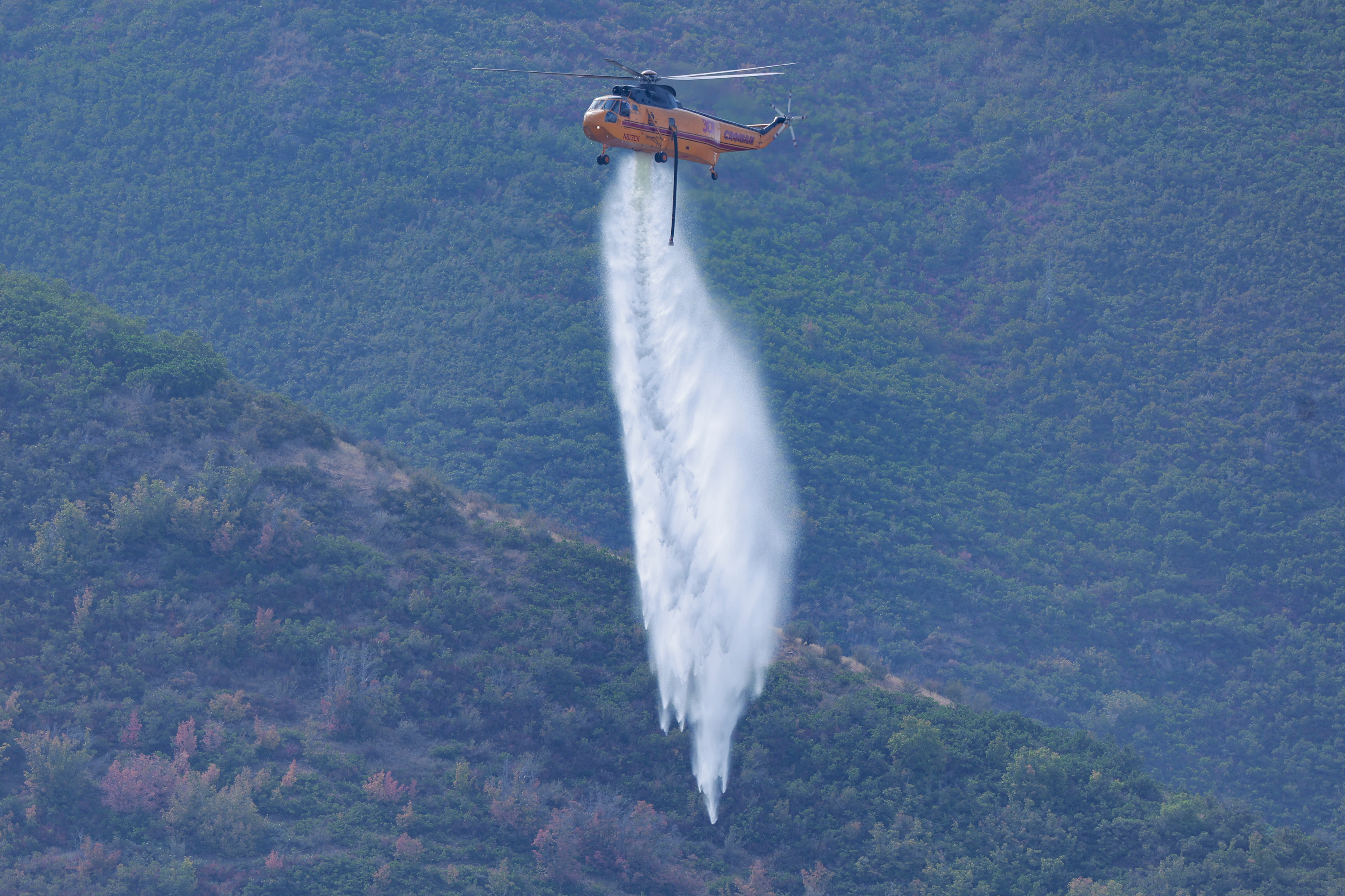 Helicopters drop water on hot spots of a fire that started on Friday Night near Mapleton on Saturday, Aug. 23, 2025.
