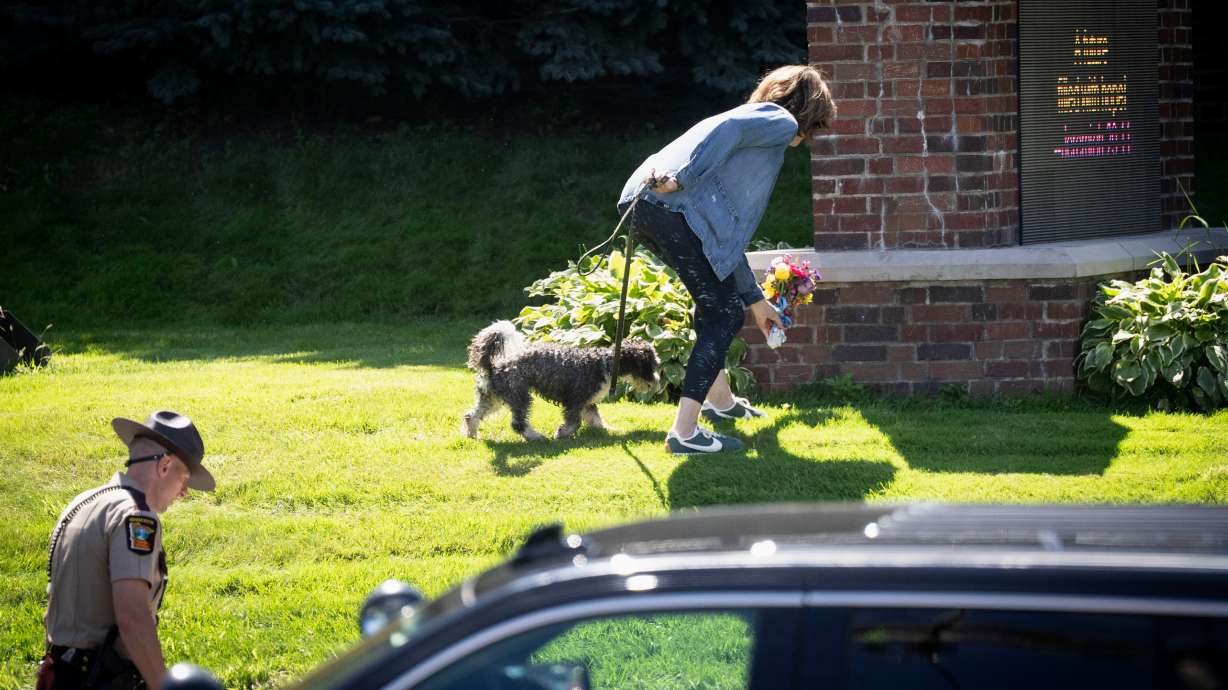 A woman is allowed to drop off flowers at the Annunciation Catholic School sign near the scene of a shooting at Annunciation Catholic Church, Wednesday in Minneapolis.