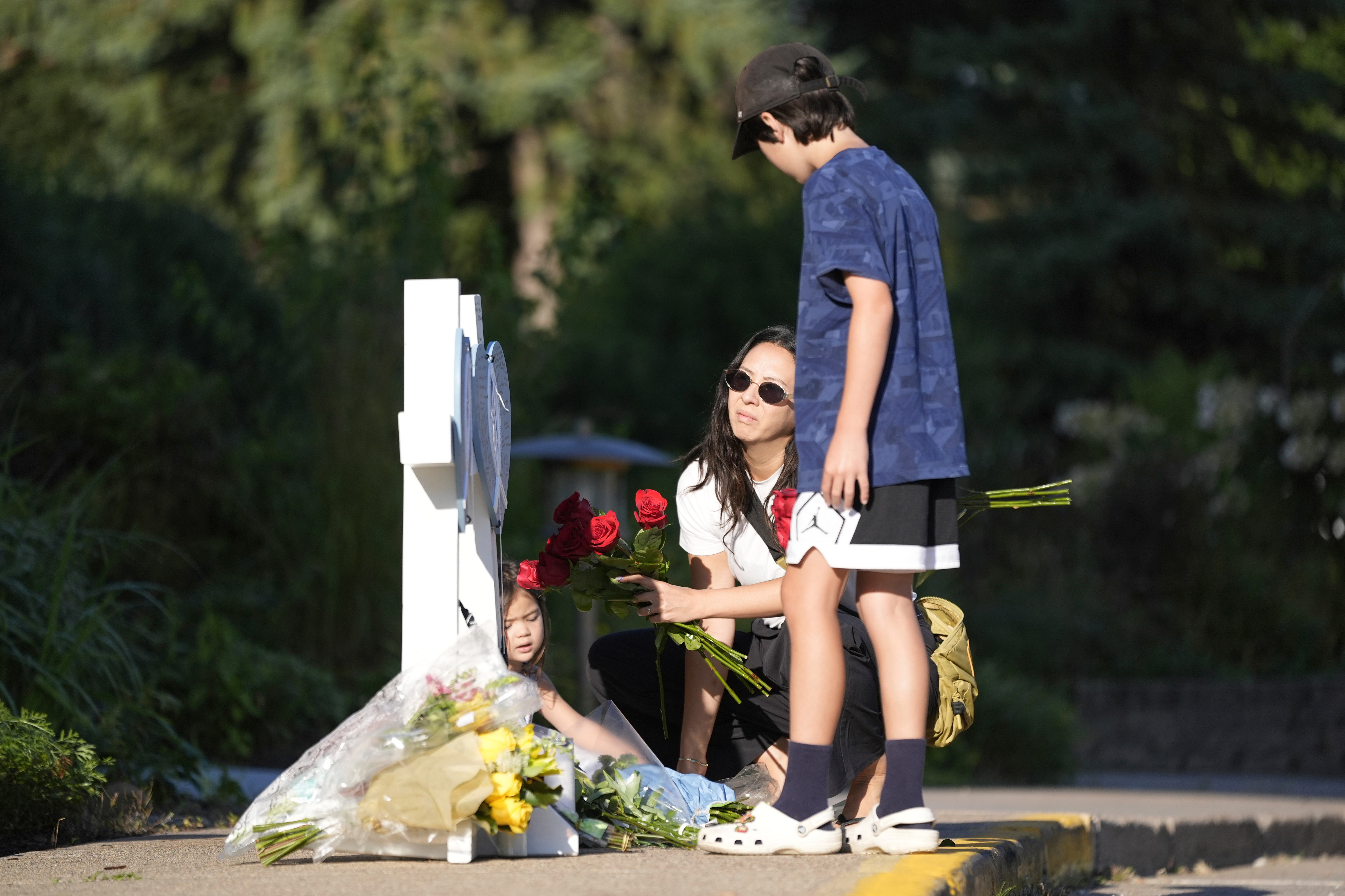 Amy Dols, and her children, Archie and Paloma place flowers at a memorial at Annunciation Catholic Church after Wednesday's school shooting, Thursday, in Minneapolis.