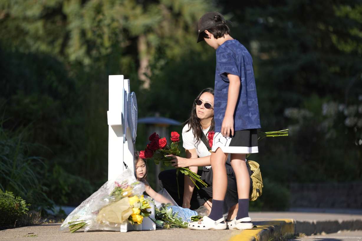 Amy Dols, and her children, Archie and Paloma place flowers at a memorial at Annunciation Catholic Church after Wednesday's school shooting, Thursday, in Minneapolis.