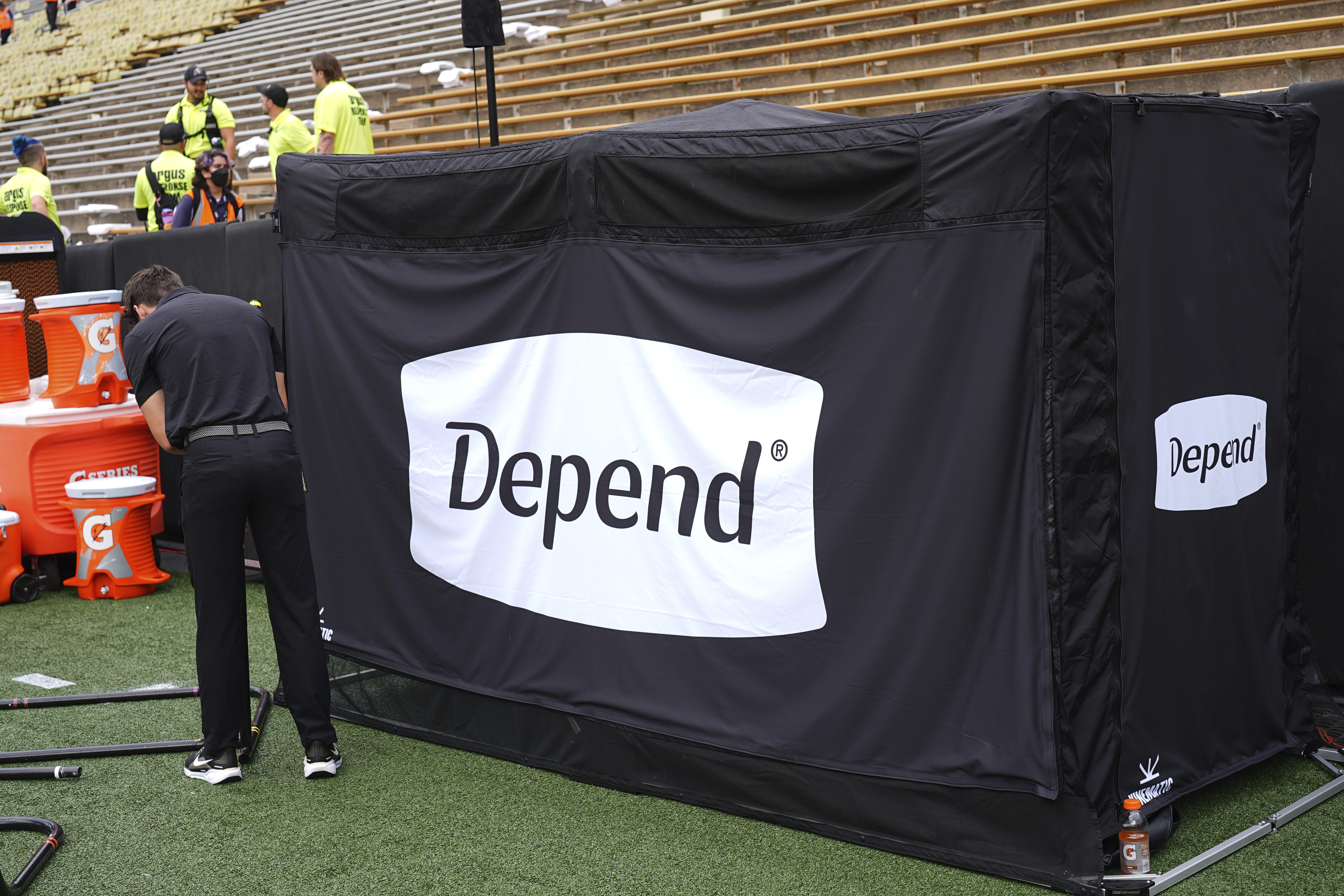 A field worker sets up equipment next to a tent containing a bathroom in the team box on the Colorado sideline before an NCAA college football game against Georgia Tech Friday, Aug. 29, 2025, in Boulder, Colo.