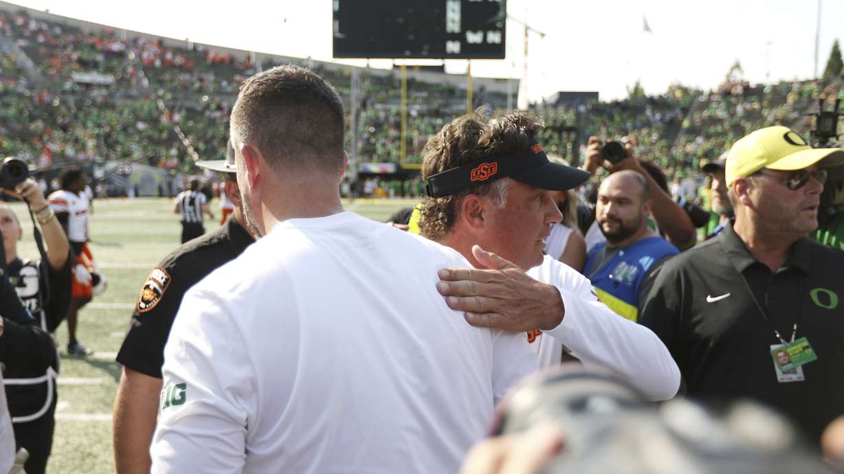 Oregon head coach Dan Lanning, left, greets Oklahoma State head coach Mike Gundy, center right, after an NCAA college football game, Saturday, Sept. 6, 2025, in Eugene, Ore.