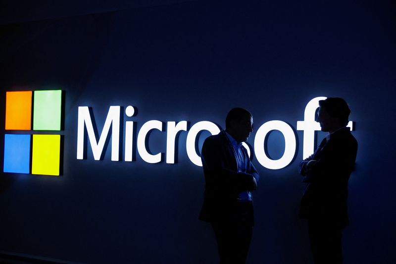 Two people talk in front of the Microsoft logo at the Mobile World Congress trade show, in Barcelona, March 3. Microsoft will require employees to work from the office at least three days a week starting next year, the company said in a blog post on Tuesday.