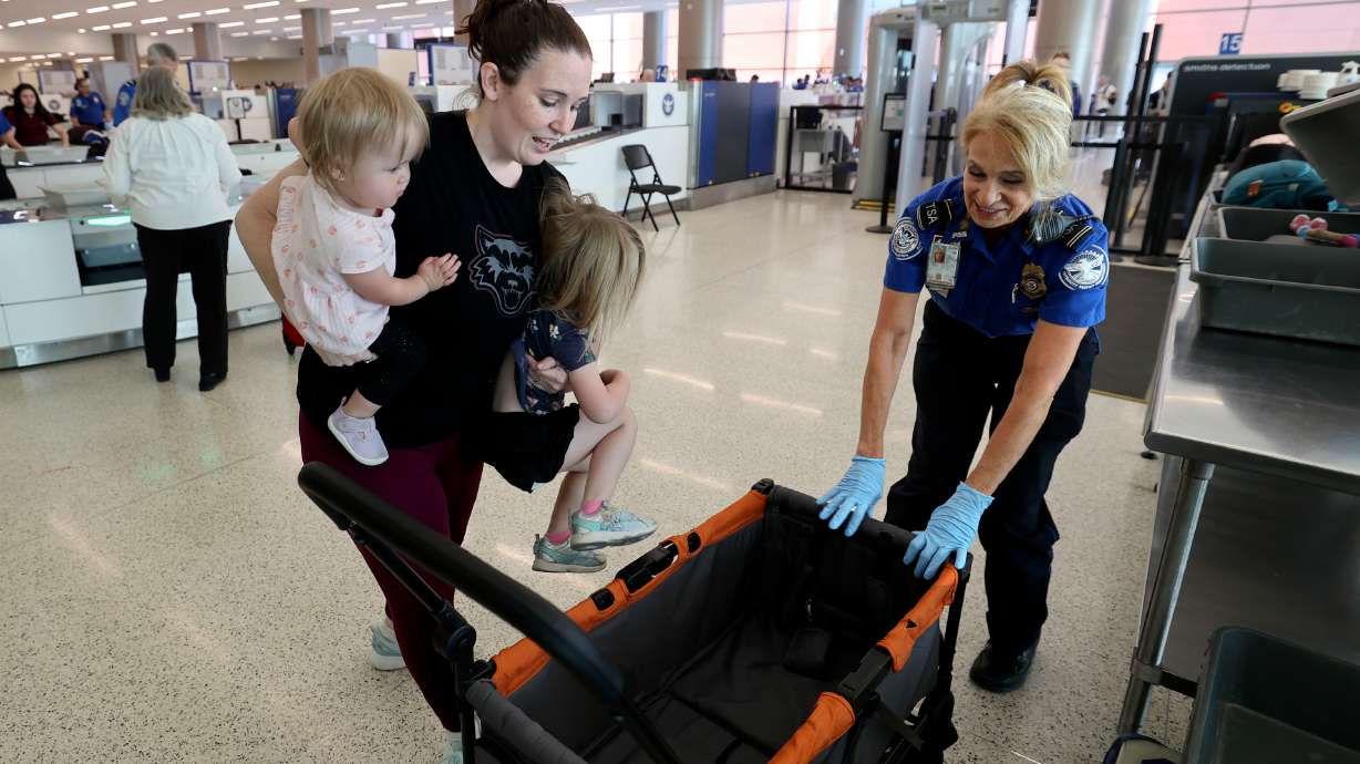 Tiffany Davis carries her daughters, Riley and Charlotte, as TSA lead officer Cyndy Riggs helps her move through the new family lane at security in the Salt Lake City International Airport in Salt Lake City on Wednesday.