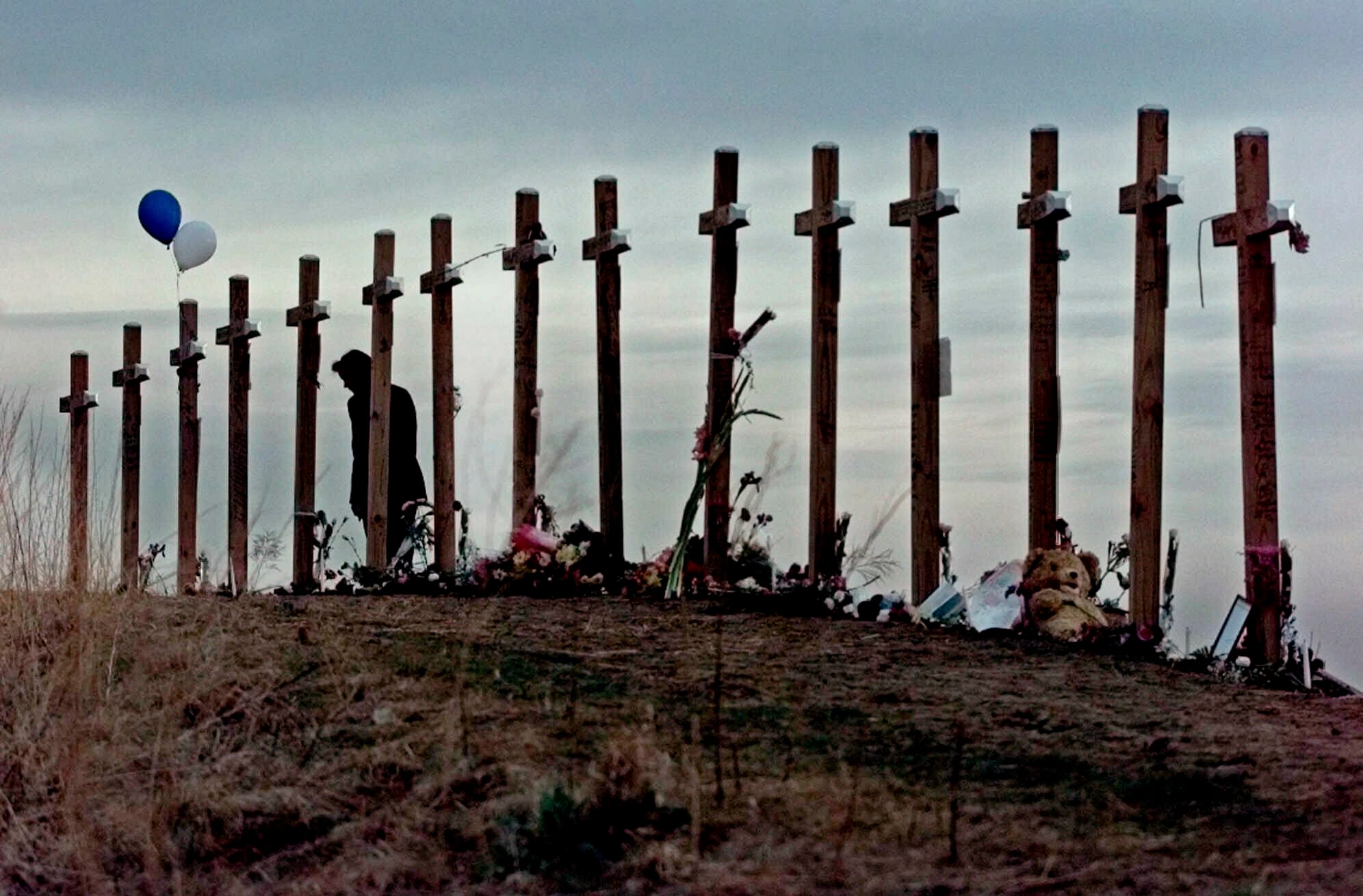 In this April 28, 1999, file photo, a woman stands among 15 crosses posted on a hill above Columbine High School in Littleton, Colo., in remembrance of the 15 people who died during a school shooting on April 20.