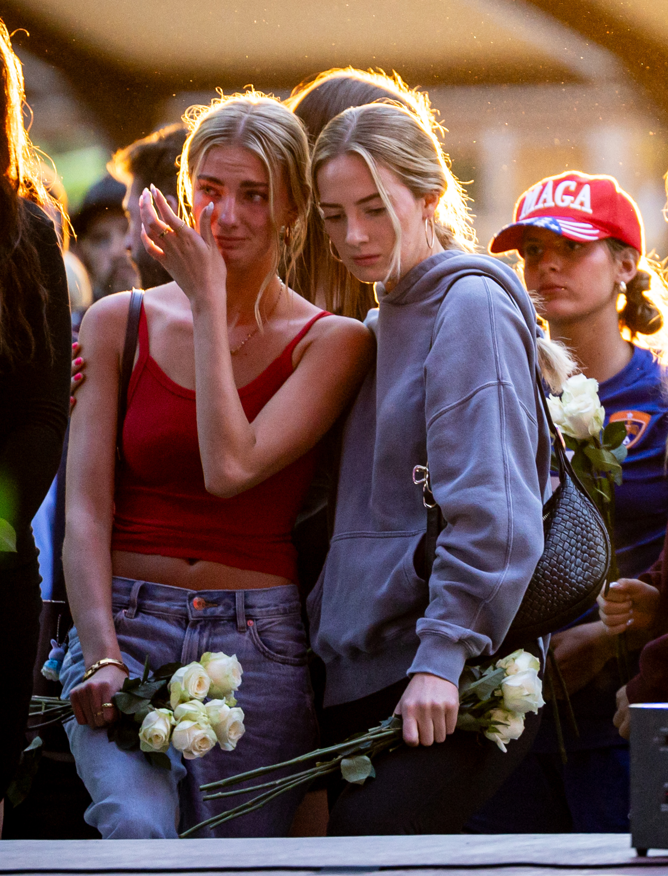 Liz Beutler, 17, left, and sister Abby Beutler, 25, right, carry flowers to place beneath Charlie Kirk’s photo at a vigil for Charlie Kirk at City Center Park in Orem on Thursday.