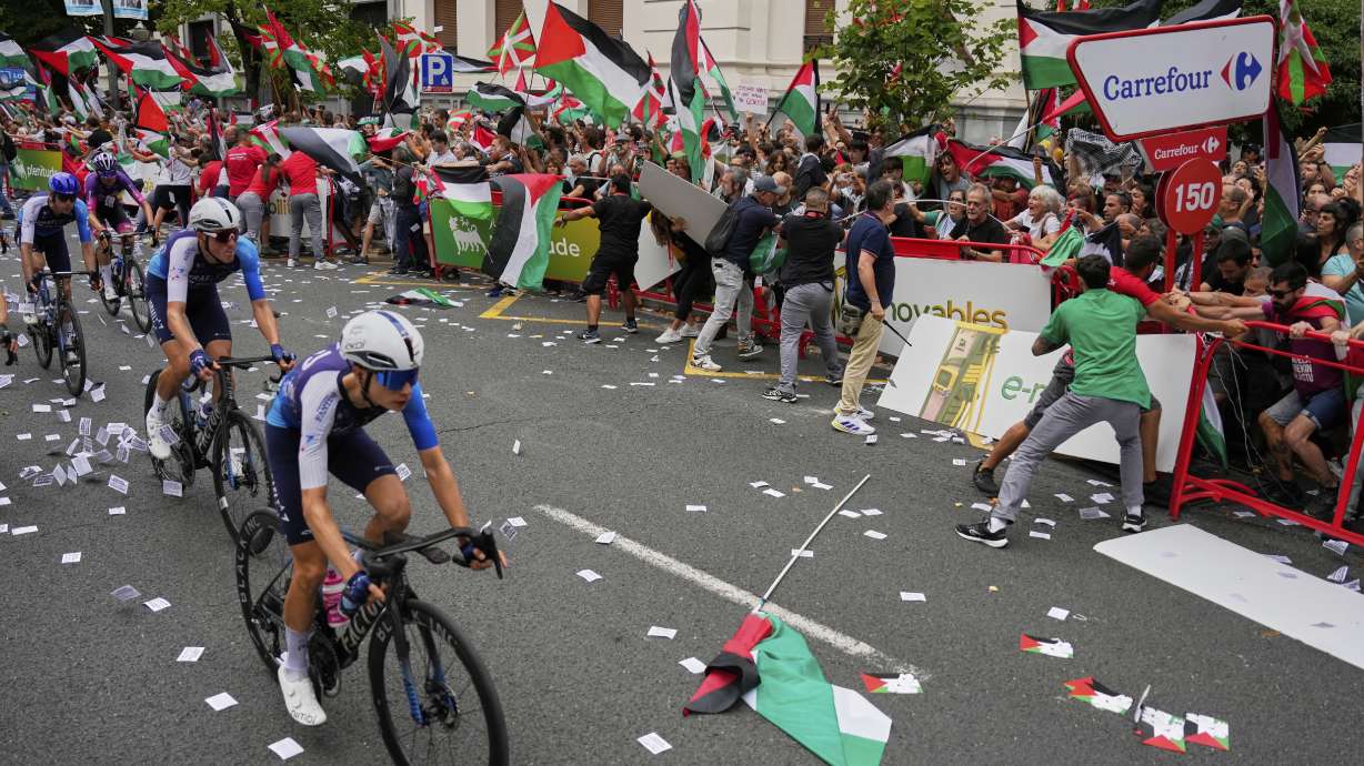 Riders of the Israel Premier Tech team compete as people holding Palestinian flags try to disrupt the eleventh stage of the Spanish Vuelta cycling race, from Bilbao to Bilbao, Spain, Wednesday, Sept. 3, 2025.