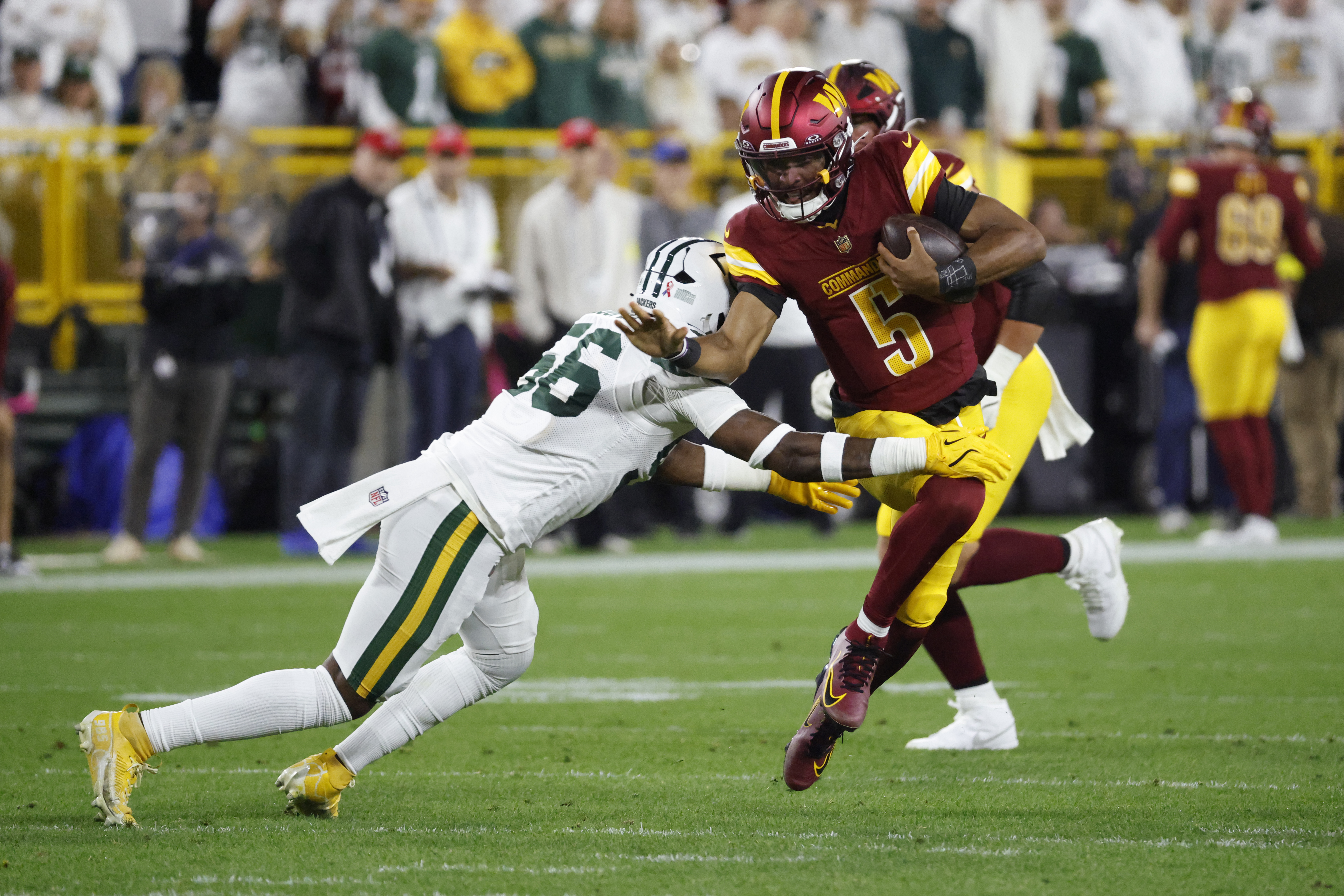 Washington Commanders quarterback Jayden Daniels (5) runs with the ball as Green Bay Packers linebacker Edgerrin Cooper (56) defends during the first half of an NFL football game Thursday, Sept. 11, 2025, in Green Bay, Wis. 