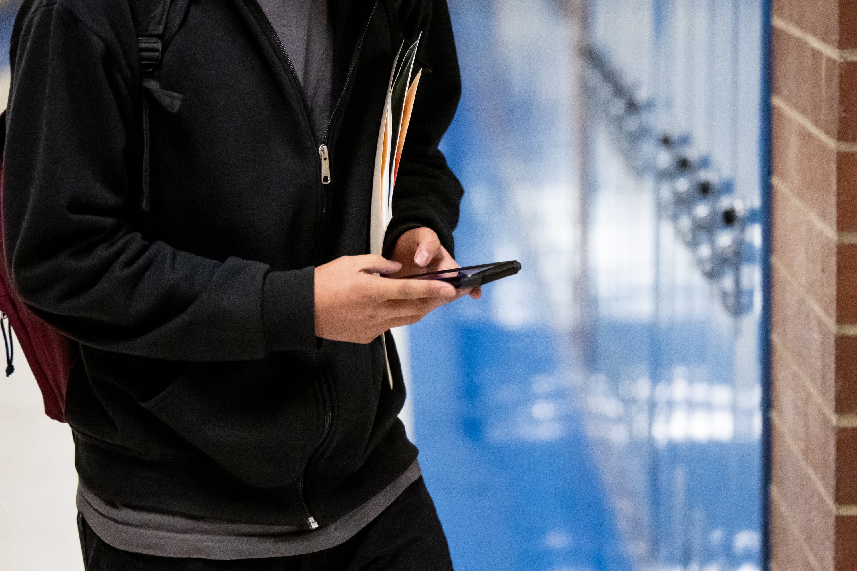 A student uses their phone while walking between classes at Cyprus High School in Magna on Jan. 27, 2023. The school’s policy allows for cellphones and other electronic devices to be used between classes, but they must be put away during class.