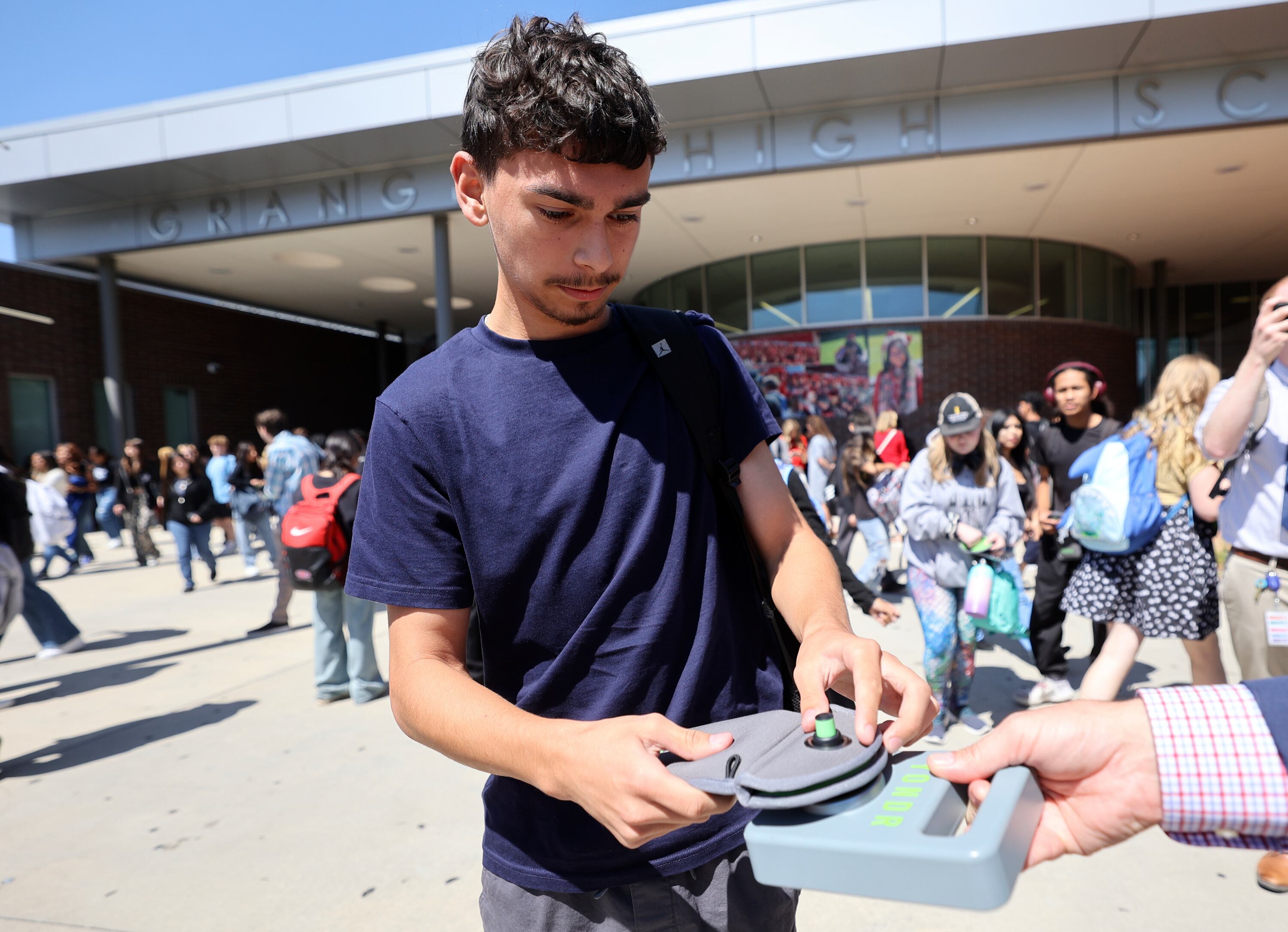 Jesse Martinez unlocks a Yondr pouch that has his cellphone inside on a magnetic unlocking base as he leaves Granger High School in West Valley City on Aug. 26, 2024. Students lock their phones in the pouches when they arrive at school, creating a phone-free learning environment.