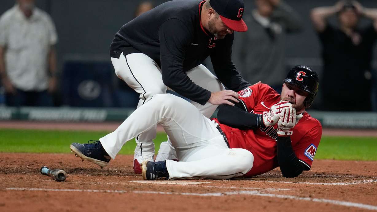 Cleveland Guardians manager Stephen Vogt, left, attends to David Fry after Fry was hit in the face with his own bunt in the sixth inning of a baseball game against the Detroit Tigers in Cleveland, Tuesday, Sept. 23, 2025.