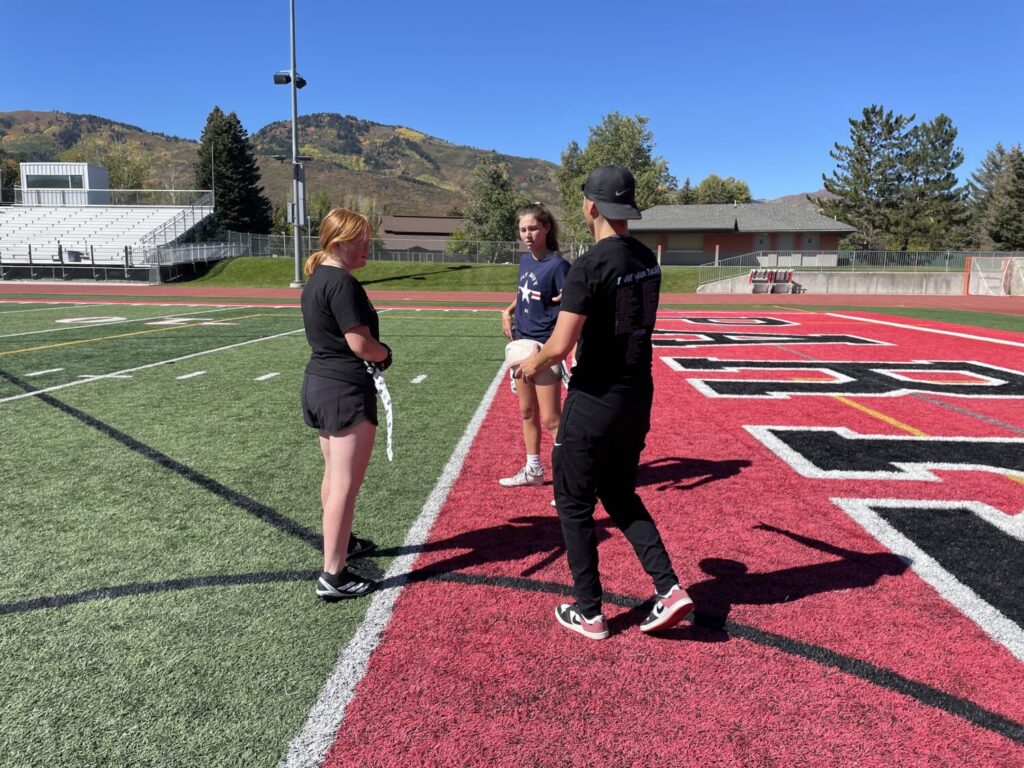 Members of the Park City High School girls' flag football team talk with co-head coach Brandon Heaney, Tuesday. Heaney, a former BYU football player, coaches the team with Erin Miller.