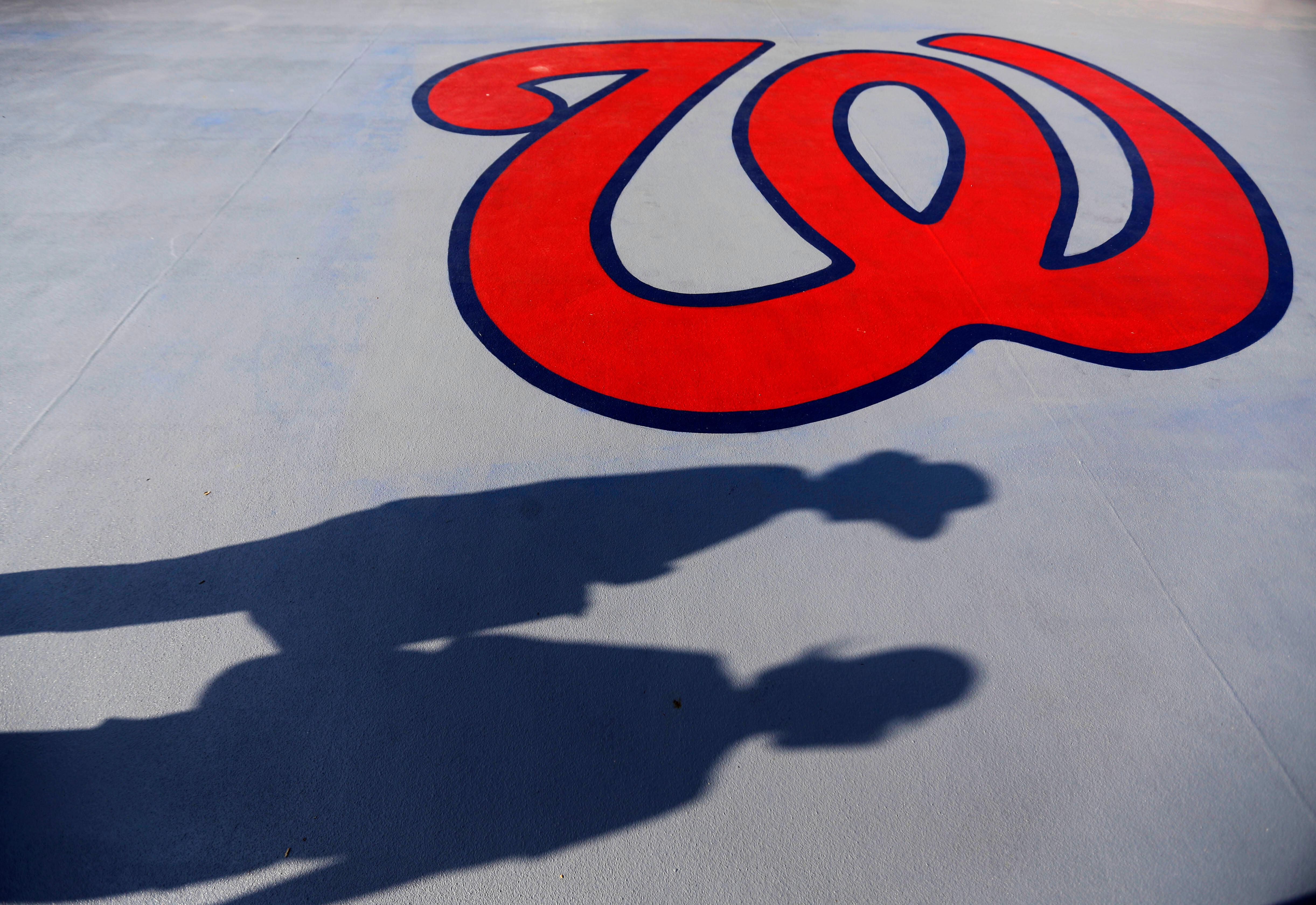 FILE - Fans cast shadows past a Washington Nationals logo as they walk in to Space Coast Stadium for an exhibition spring training baseball game between the Nationals and the New York Mets, Thursday, March 5, 2015, in Viera, Fla. 