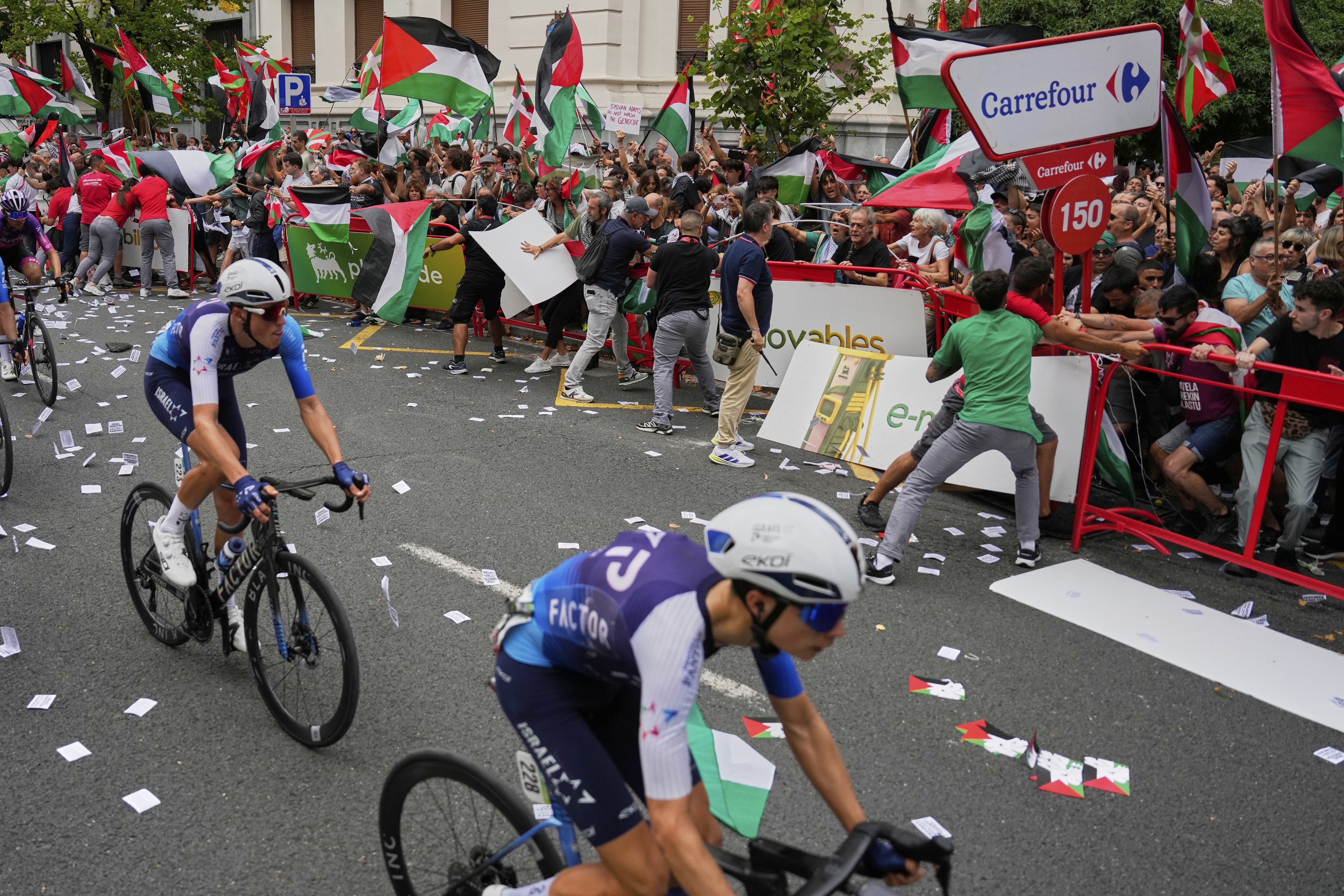 Riders of the Israel Premier Tech team compete as people holding Palestinian flags try to disrupt the eleventh stage of the Spanish Vuelta cycling race, from Bilbao to Bilbao, Spain, Wednesday, Sept. 3, 2025. 