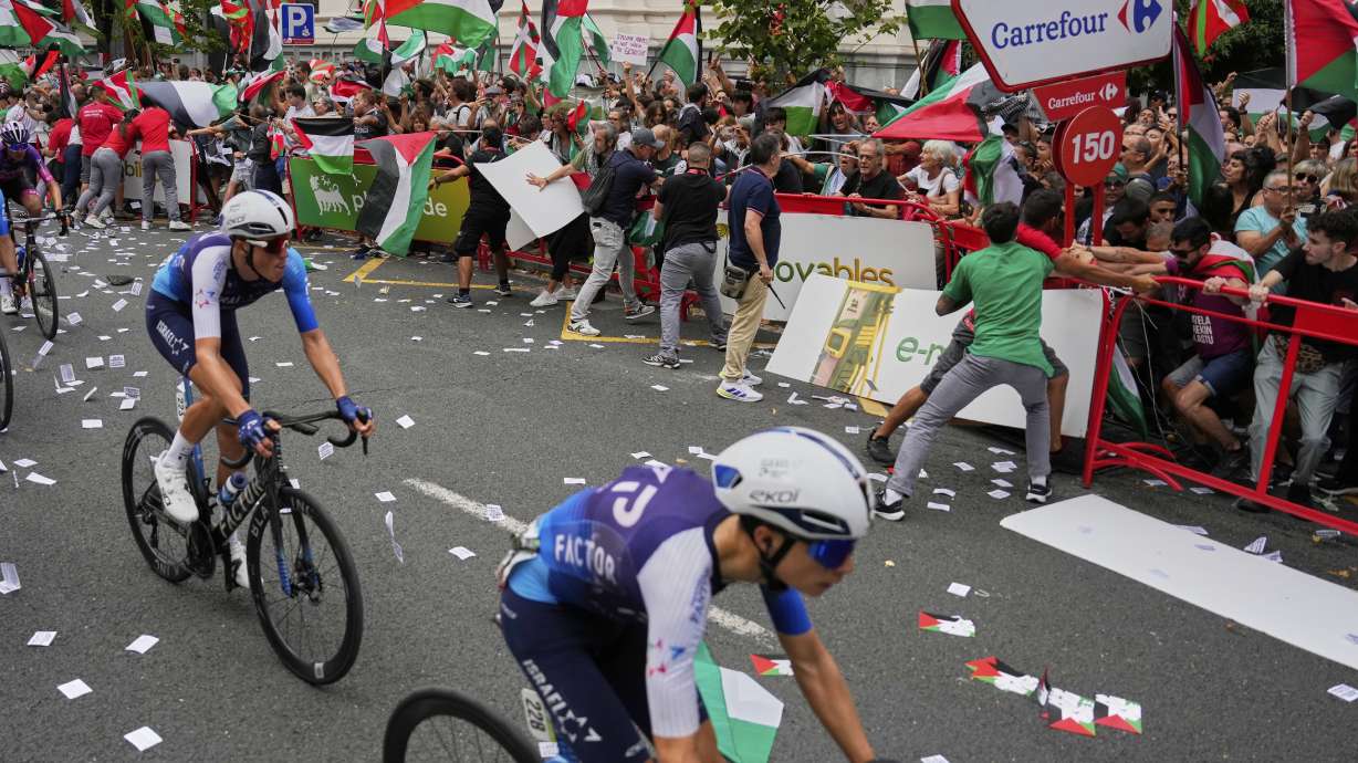 Riders of the Israel Premier Tech team compete as people holding Palestinian flags try to disrupt the eleventh stage of the Spanish Vuelta cycling race, from Bilbao to Bilbao, Spain, Wednesday, Sept. 3, 2025.