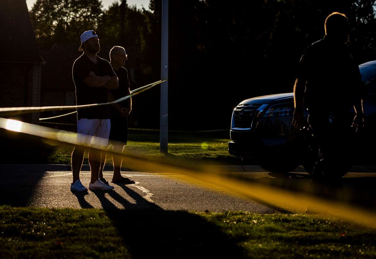 Blake Lang, left, looks on from behind crime scene tape, hours after a shooting and fire at a meetinghouse of The Church of Jesus Christ of Latter-day Saints in Grand Blanc Township, Michigan, on Sunday. Lang lives nearby.
