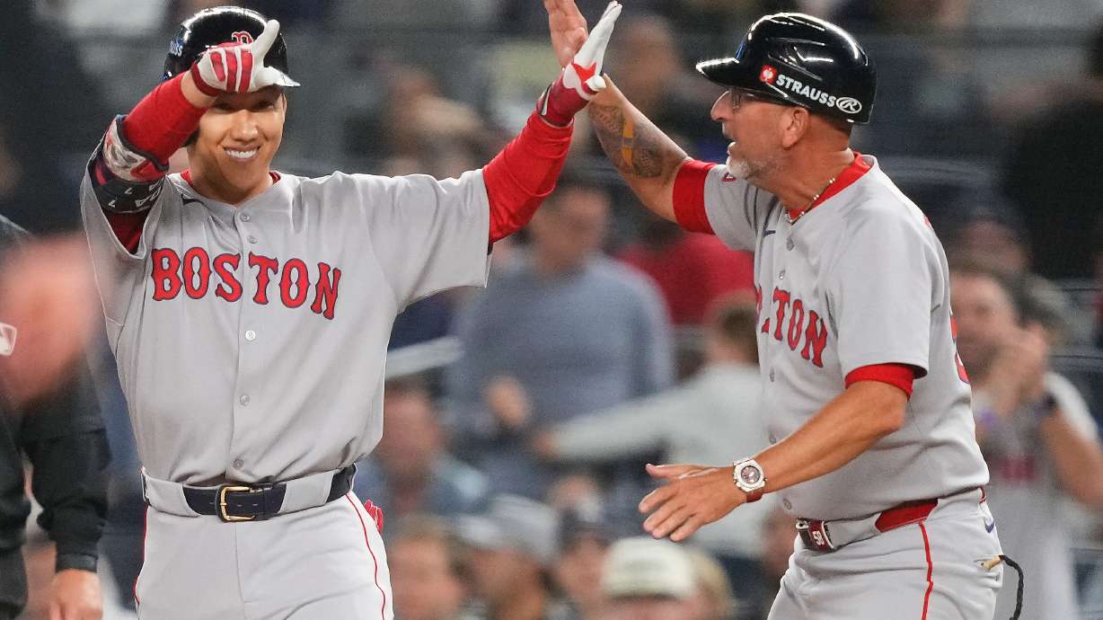 Boston Red Sox outfielder Masataka Yoshida, left, celebrates with first base coach José David Flores after driving in two runs against the New York Yankees during the seventh inning of Game 1 of an American League wild-card baseball playoff series, Tuesday, Sept. 30, 2025, in New York.