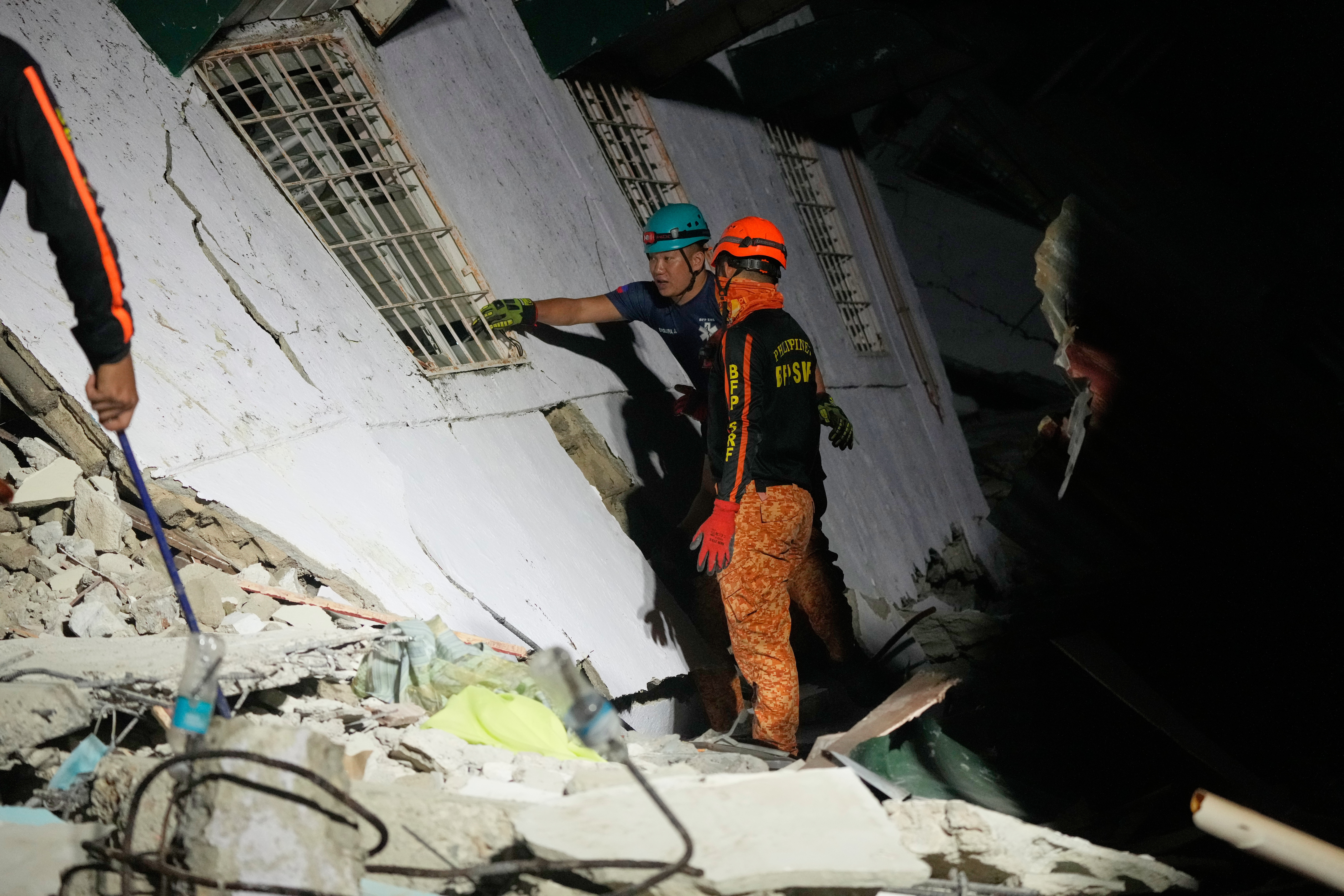Rescuers check for survivors from the ruins of a collapsed building, Wednesday, after a strong earthquake struck Bogo in the Philippines. Traumatized residents remained outdoors despite intermittent rain following the temblor.