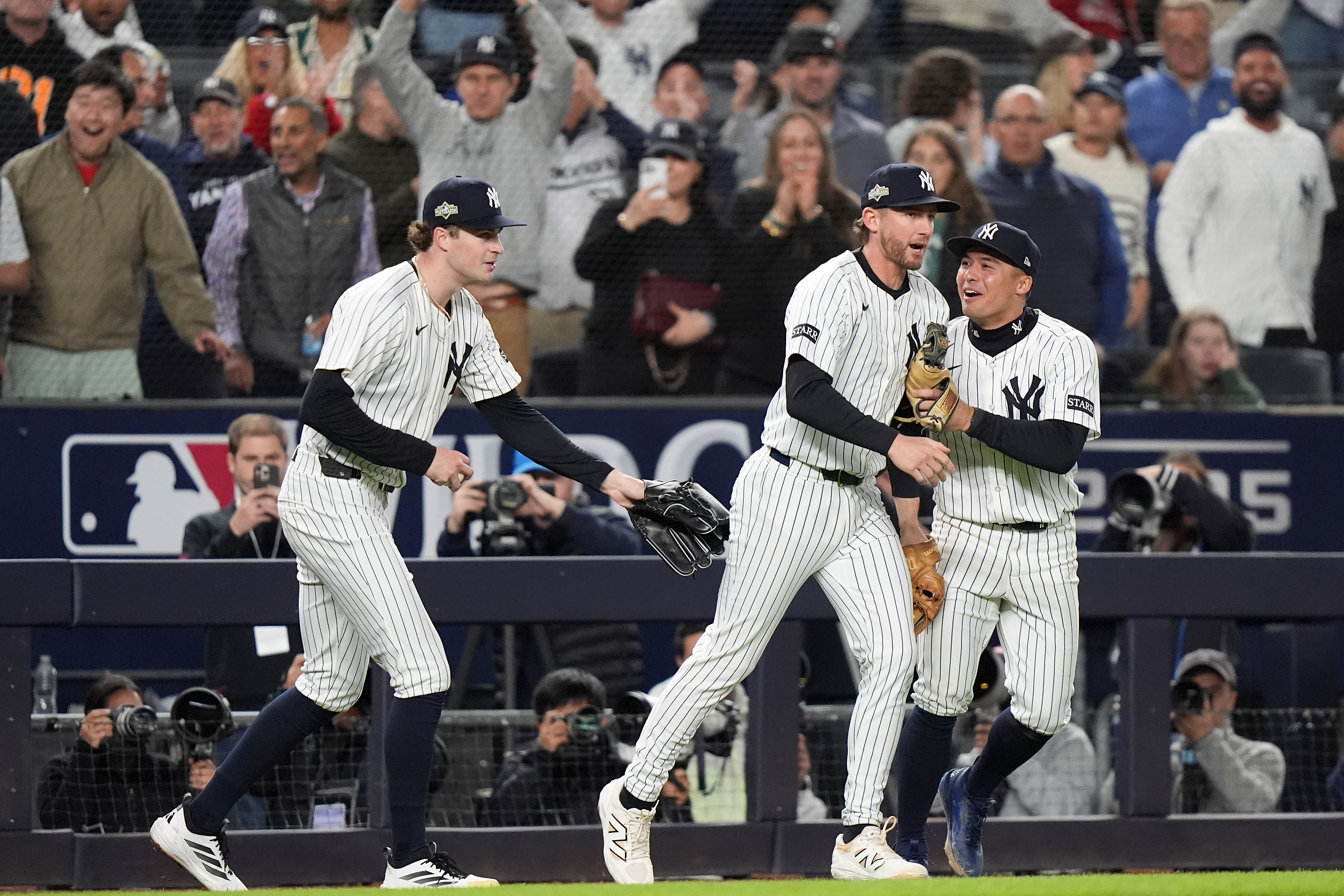 New York Yankees third base Ryan McMahon, center, is congratulated by pitcher Cam Schlittler, left, and shortstop Anthony Volpe after making a catch over the Boston Red Sox dugout during the eighth inning of Game 3 of an American League wild-card baseball playoff series, Thursday, Oct. 2, 2025, in New York.