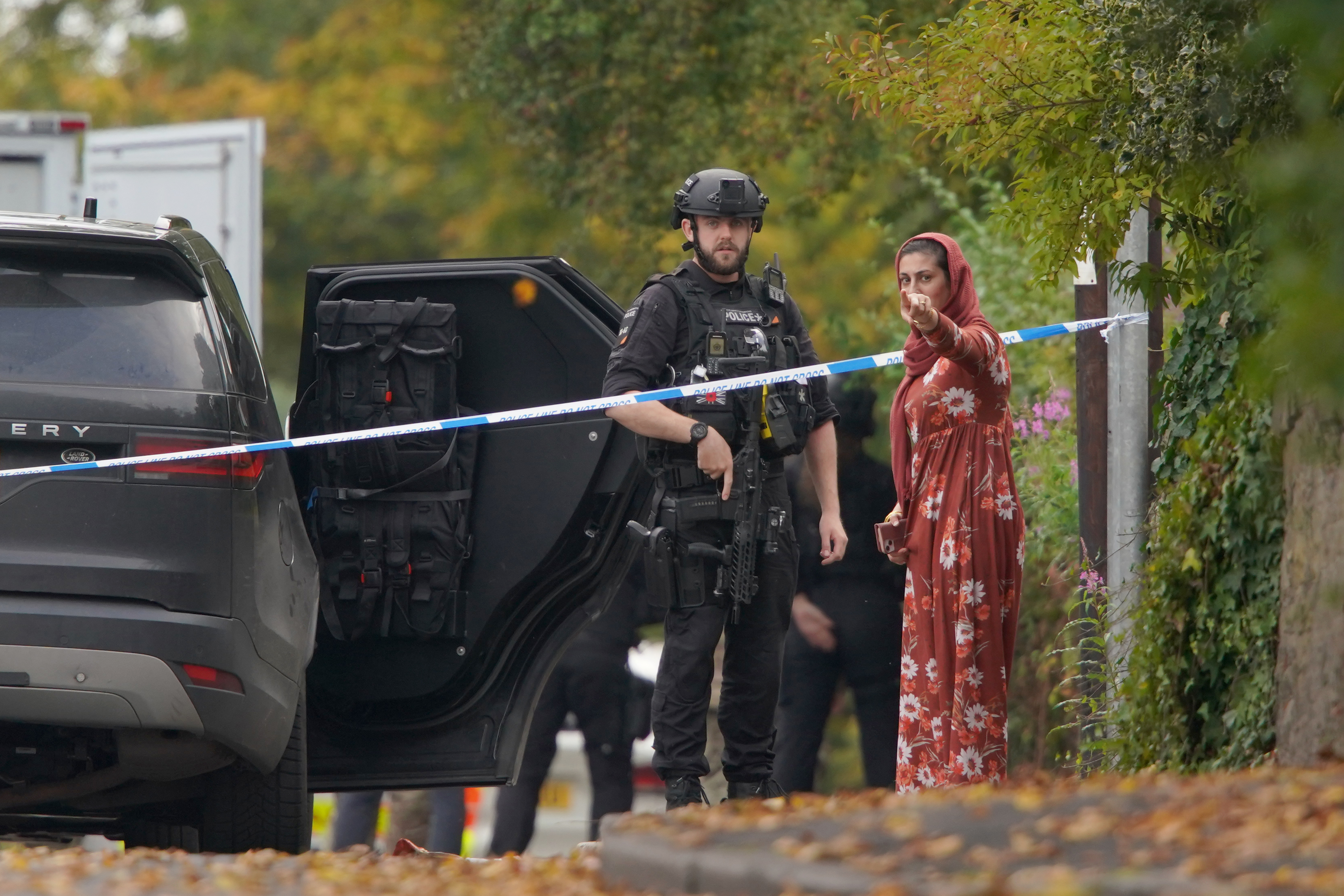Police speak to member of the public near the scene of a stabbing incident in Crumpsall, Manchester, England, Thursday. Authorities said Friday that one of the victims in the attack may have been accidentally shot by police.