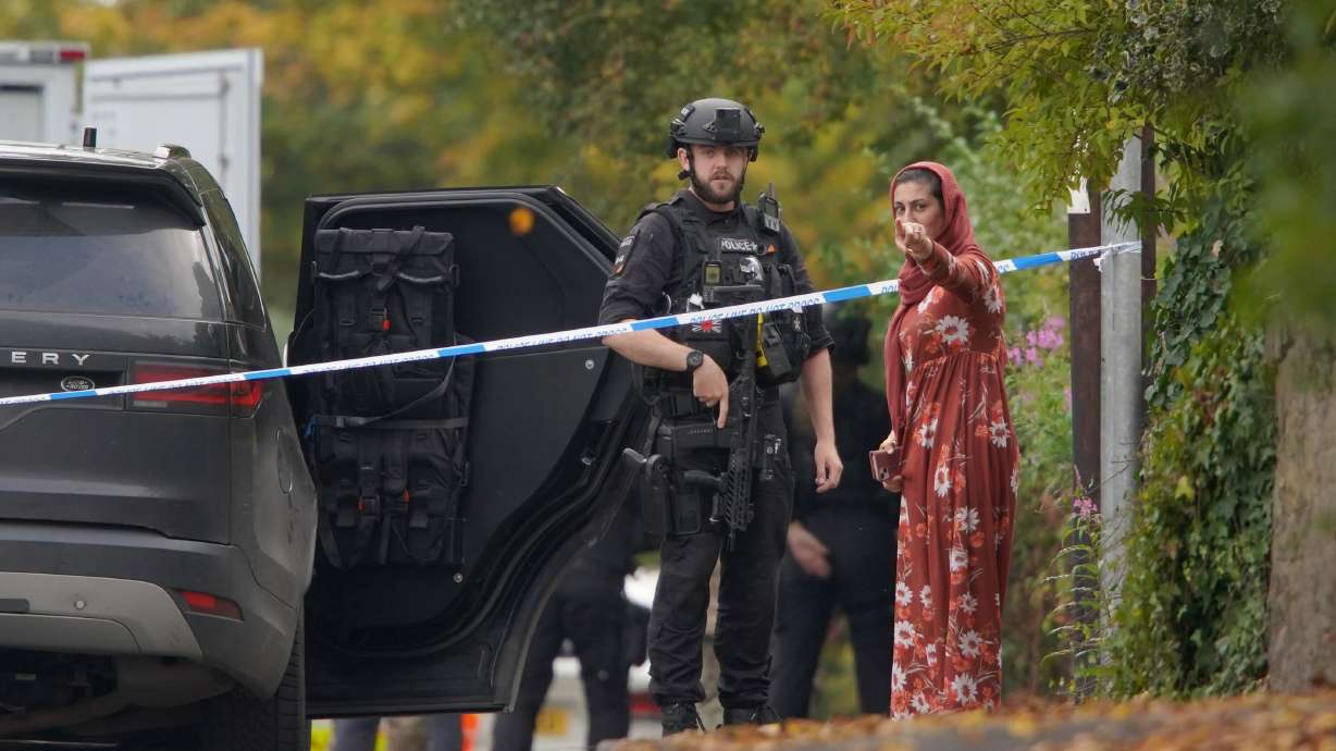 Police speak to member of the public near the scene of a stabbing incident in Crumpsall, Manchester, England, Thursday. Authorities said Friday that one of the victims in the attack may have been accidentally shot by police.