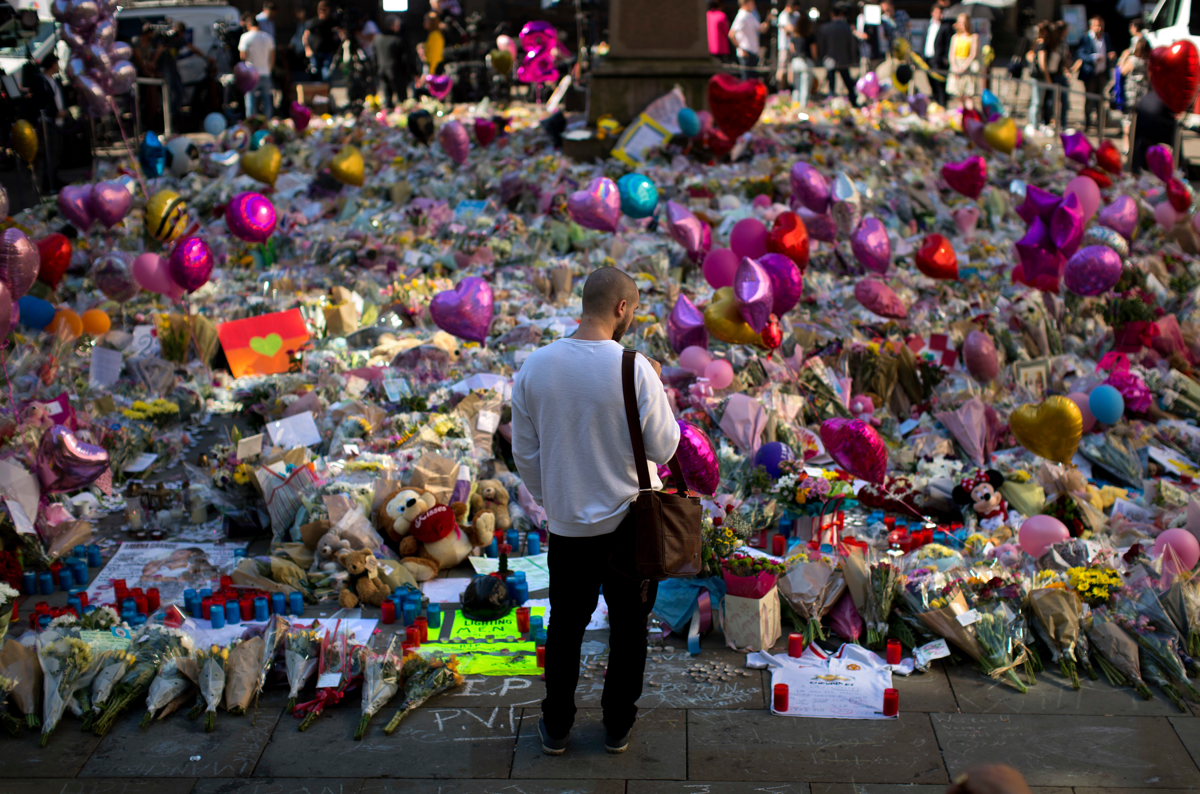 FILE - A man stands next to flowers for the victims of a bombing at St. Ann's Square in central Manchester, England, May 26, 2017. 