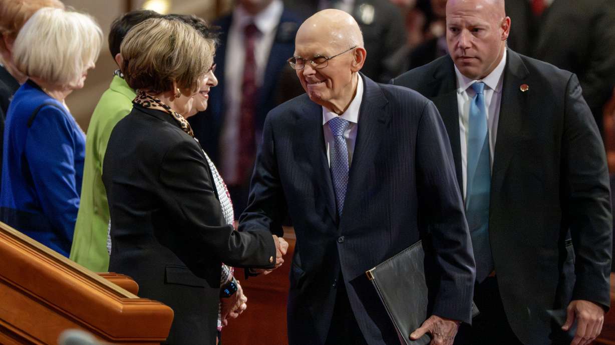 President Dallin H. Oaks, president of the Quorum of the Twelve Apostles, shakes hands and scrunches his face at his wife, Sister Kristen M. Oaks, as he takes his place on the stand for afternoon session of the 195th Semiannual General Conference of The Church of Jesus Christ of Latter-day Saints at the Conference Center in Salt Lake City on Sunday.