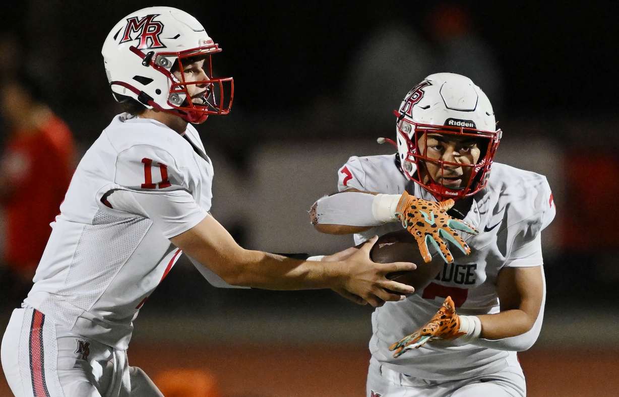 Mountain Ridge’s Jaxon Hunt hands the ball off to Zach Ofisa as they play at Herriman on Friday, Oct. 3, 2025. The game was delayed part way through the third quarter, due to lightning.