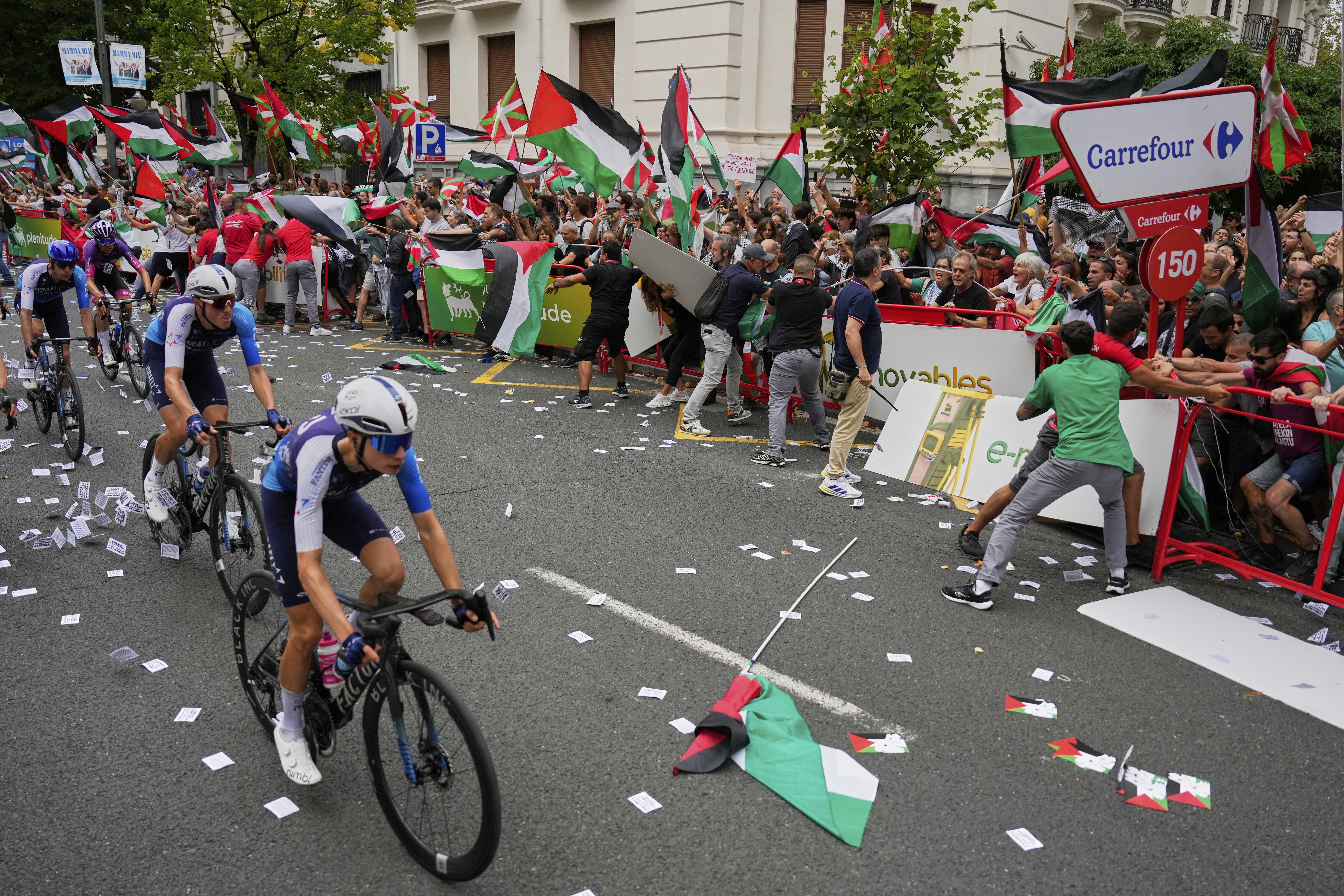 Riders of the Israel Premier Tech team compete as people holding Palestinian flags try to disrupt the eleventh stage of the Spanish Vuelta cycling race, from Bilbao to Bilbao, Spain, Wednesday, Sept. 3, 2025. 