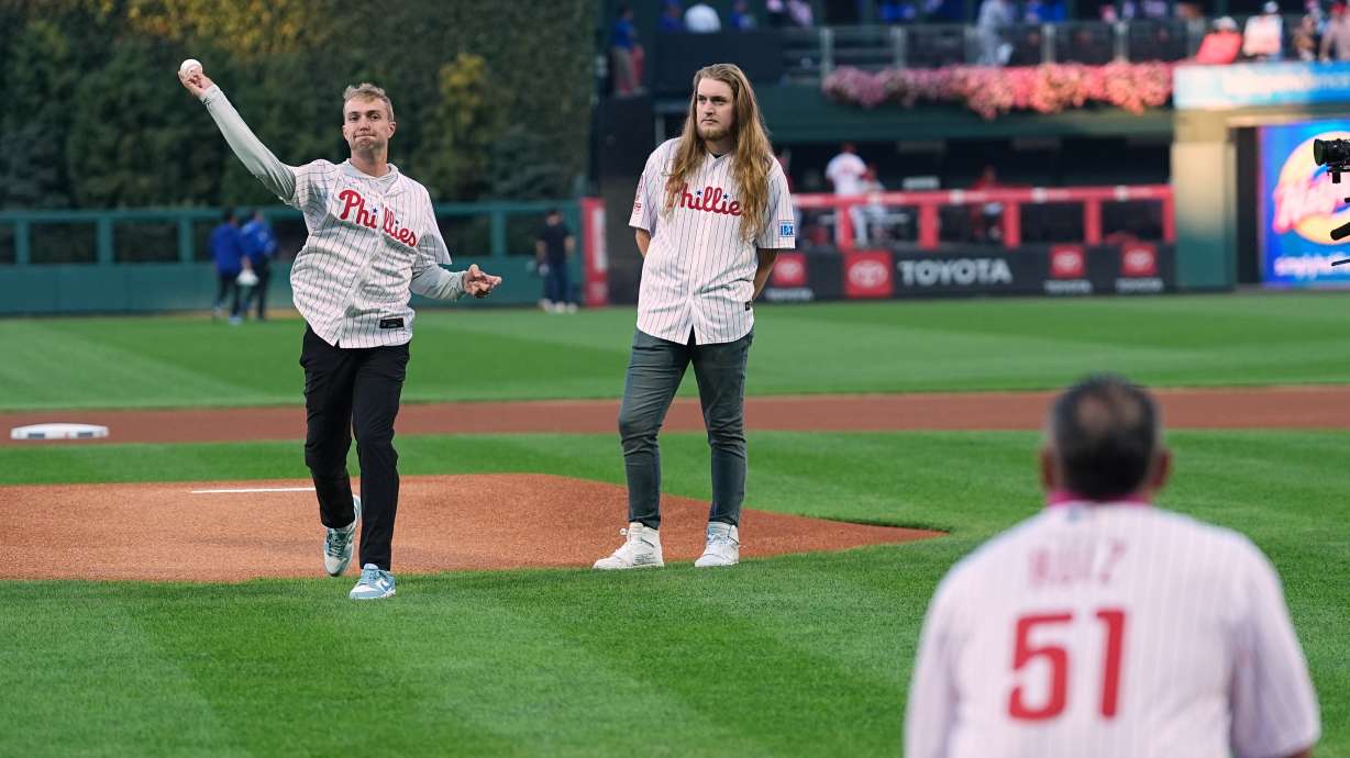 CORRECTS FIRST NAME TO RYAN, NOT MATT - Braden Halladay, left, accompanied by his brother Ryan Halladay, throws a ceremonially first pitch to former Philadelphia Phillies catcher Carlos Ruiz, marking the 15th anniversary of their father Roy Halladay's postseason no-hitter, ahead of Game 2 of baseball's National League Division Series between the Phillies and the Los Angeles Dodgers, Monday, Oct. 6, 2025, in Philadelphia.