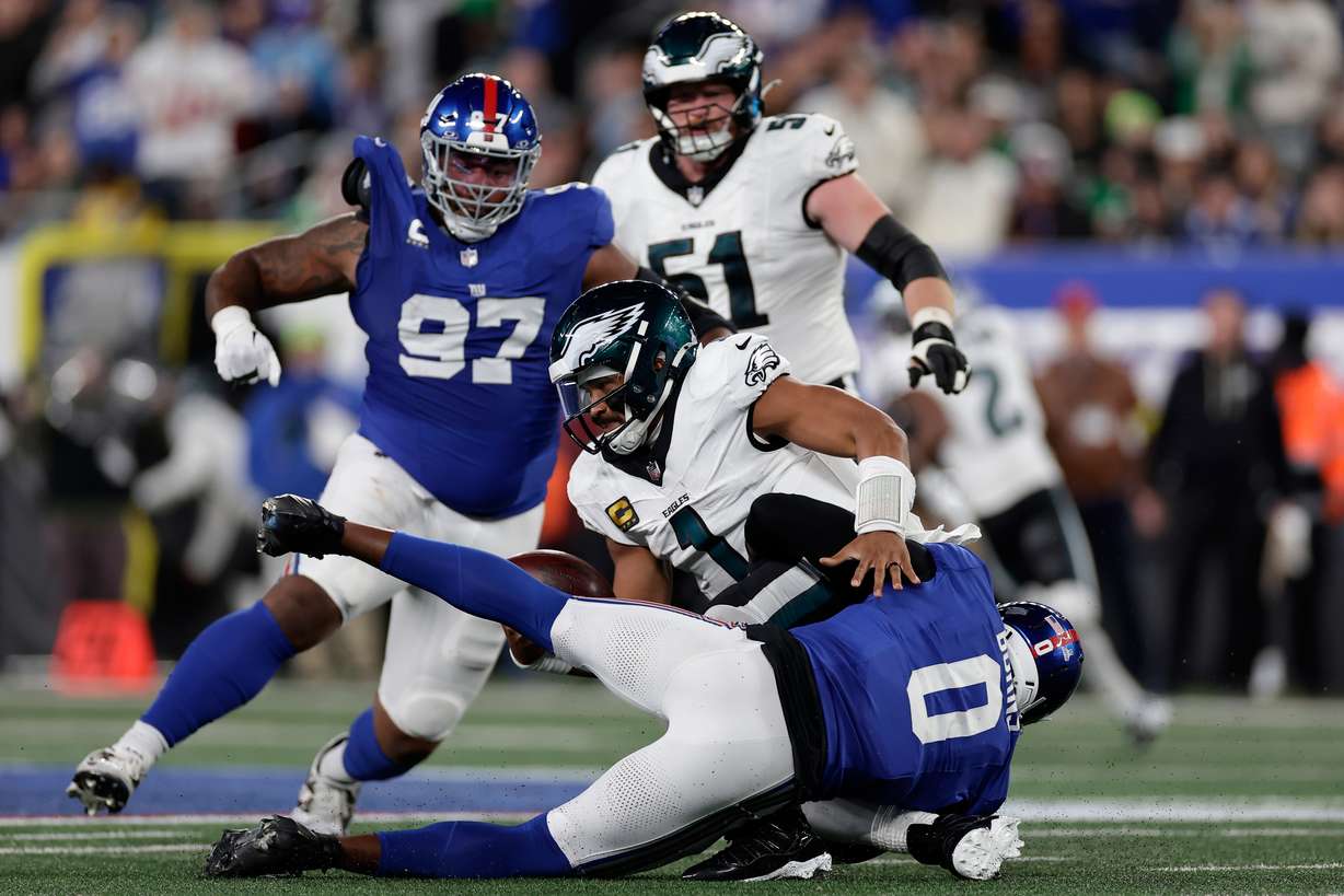Philadelphia Eagles' Jalen Hurts (1) is sacked by New York Giants' Brian Burns (0) during the second half of an NFL football game Thursday, Oct. 9, 2025, in East Rutherford, N.J.