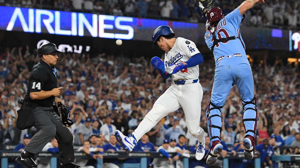 Los Angeles Dodgers' Hyeseong Kim, center, scores the game-winning run past Philadelphia Phillies catcher J.T. Realmuto (10) on a ground ball by Andy Pages and a throwing error by Phillies pitcher Orion Kerkering during the eleventh inning in Game 4 of baseball's National League Division Series Thursday, Oct. 9, 2025, in Los Angeles.
