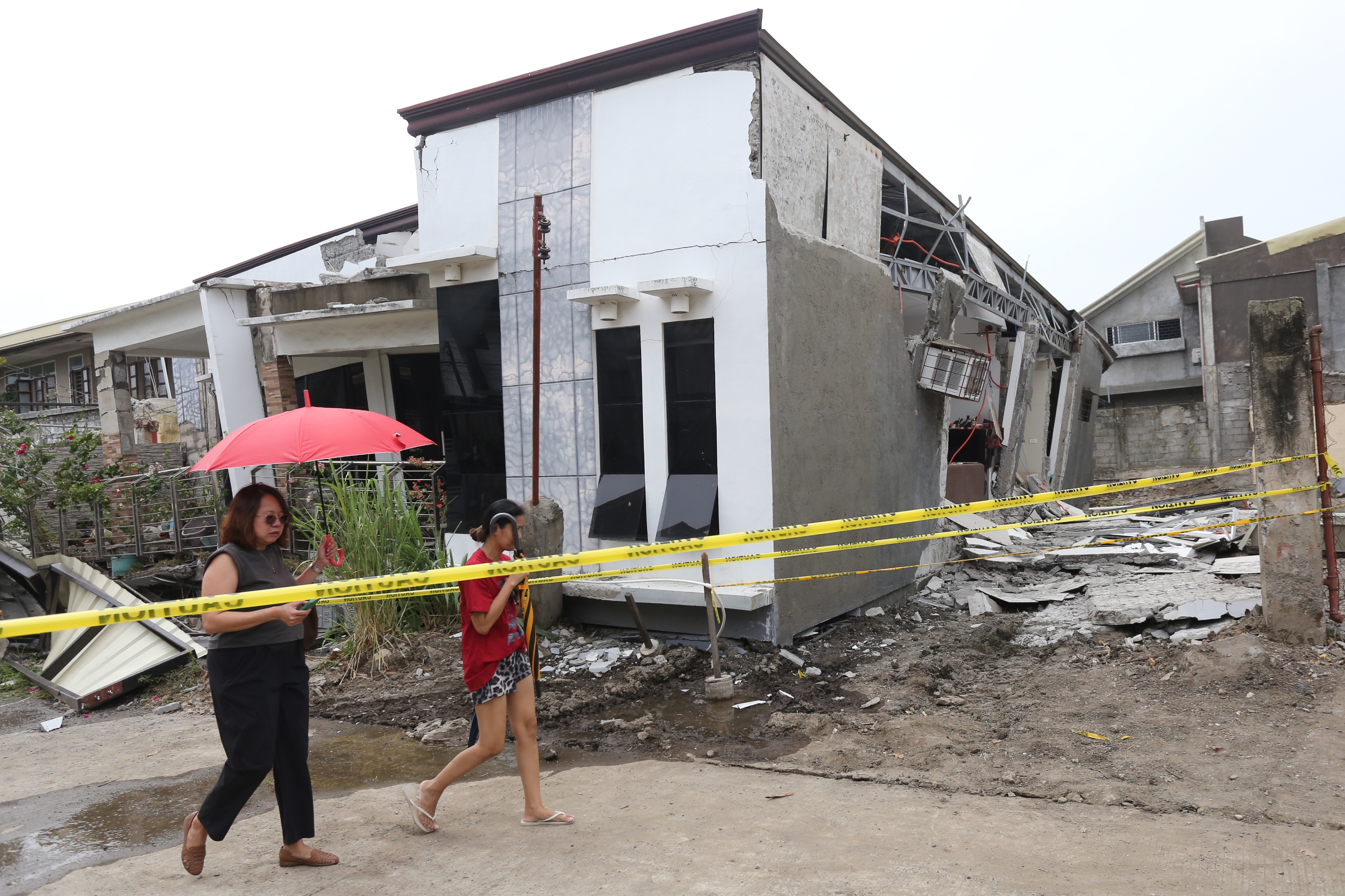 Two women walk past a damaged house after a strong earthquake in Davao City, southern Philippines on Friday.