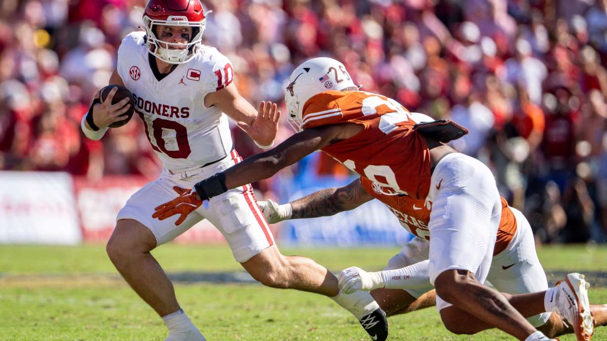 Oklahoma quarterback John Mateer, left, tries to avoid a tackle by Texas linebacker Ty'Anthony Smith (26) as he scrambles during the first half of an NCAA college football game Saturday, Oct. 11, 2025, in Dallas.