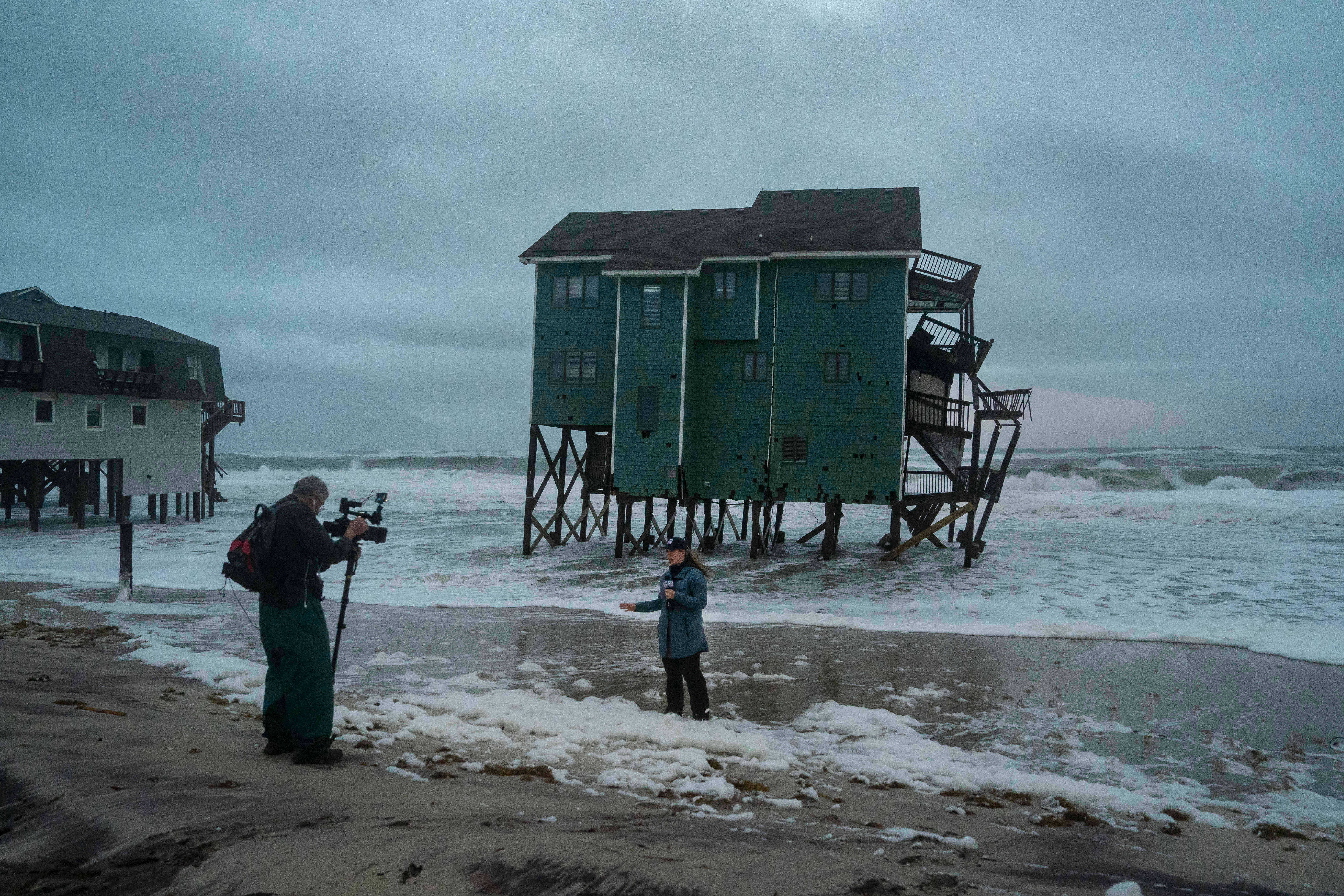 A Fox Weather reporter films in front of a house at risk of collapse in the midst of a storm, Sunday, in Buxton, N.C.