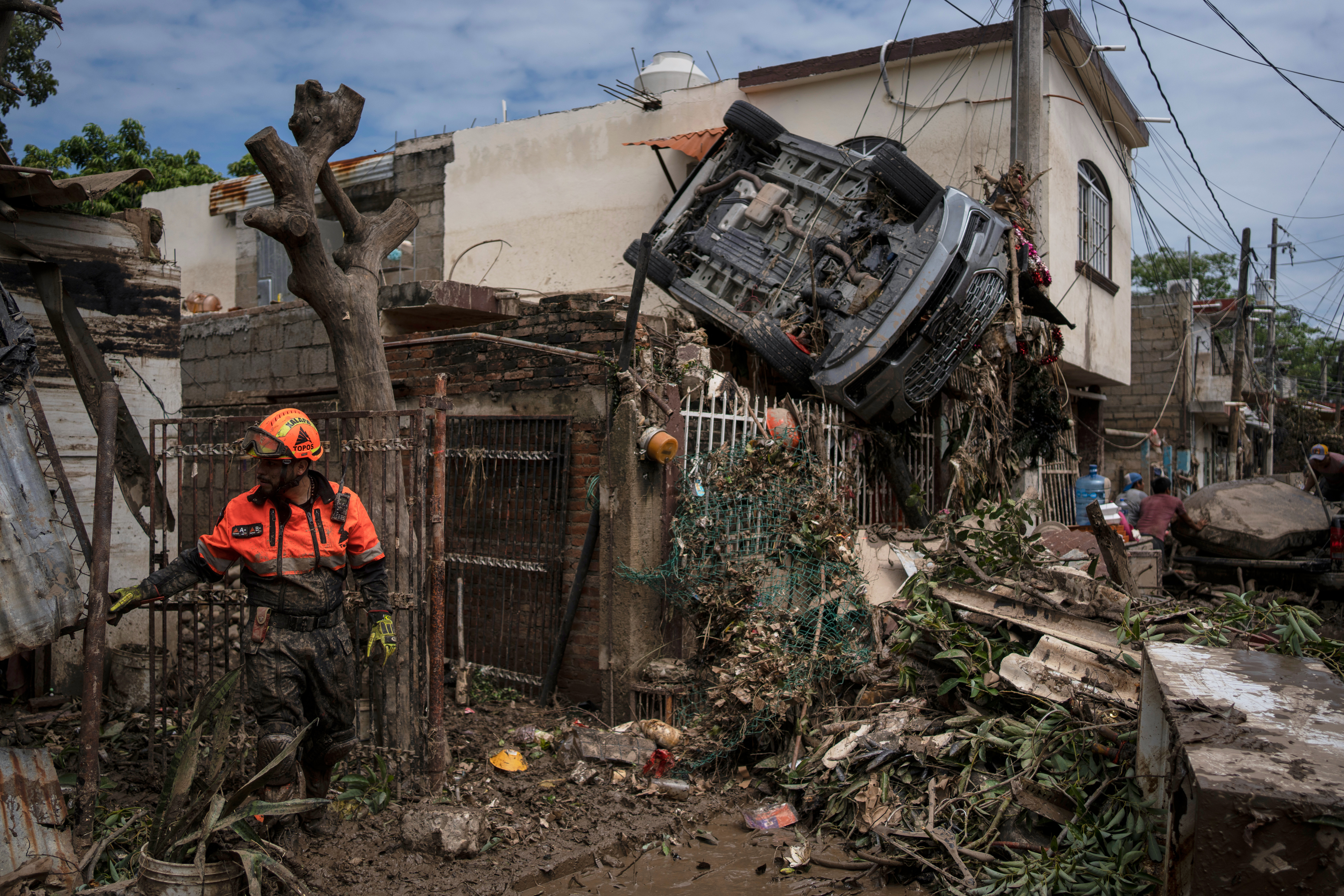 A rescue worker works near a car hanging over a fence by a damaged house in Poza Rica, Mexico, Monday, after torrential rains. A river turned into a crushing wall of water that wiped the village of Chapula off the map and affected several other areas.