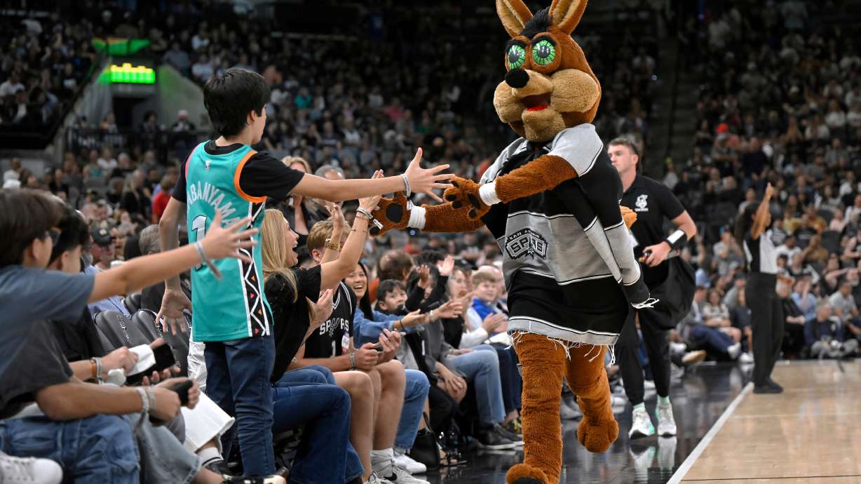 FILE - The Coyote, right, San Antonio Spurs' mascot, greets fans during the second half of an NBA basketball game against the Minnesota Timberwolves, Saturday, Nov. 2, 2024, in San Antonio. San Antonio won 113-103.