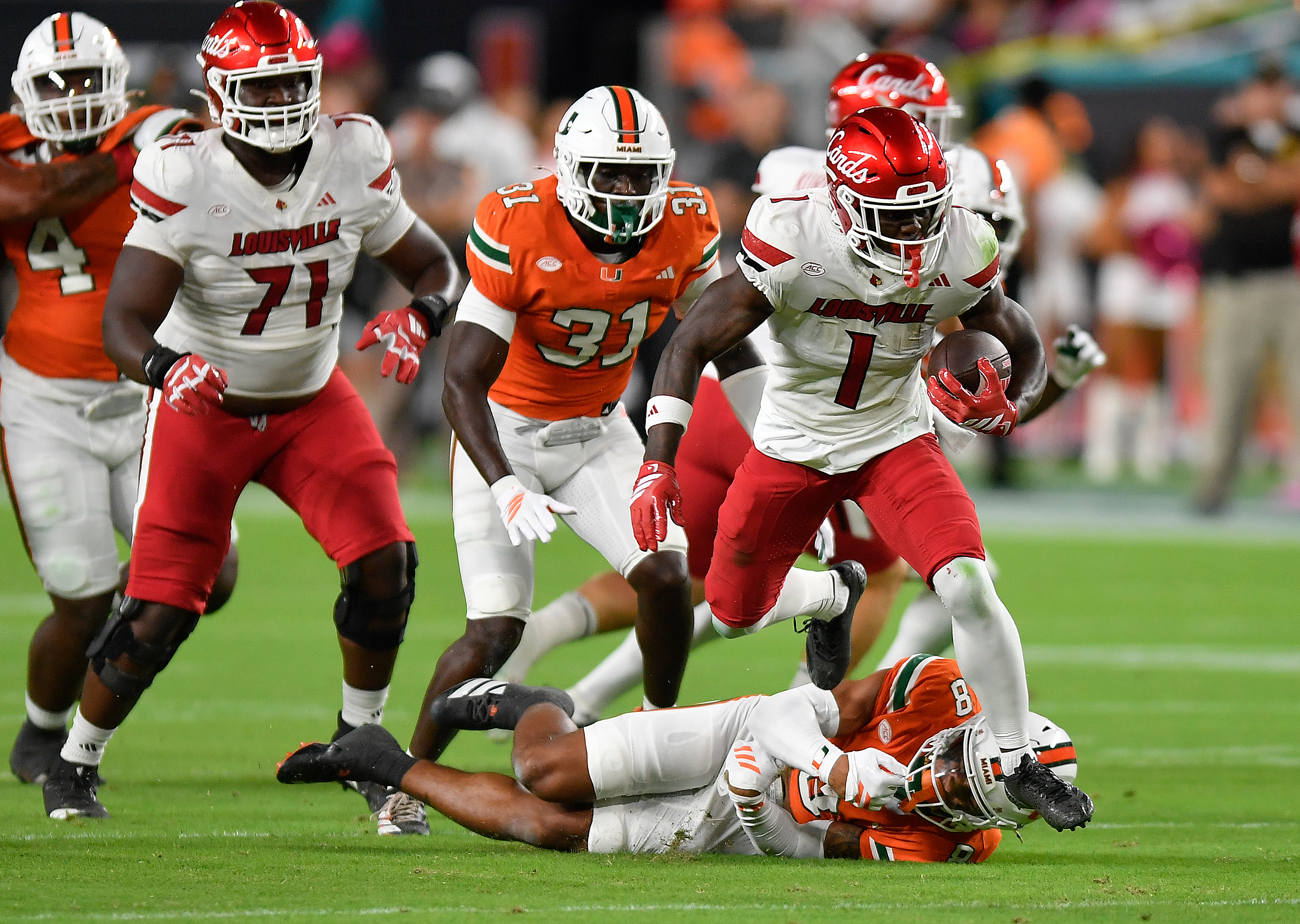 Louisville running back Isaac Brown (1) runs over Miami defensive back Jakobe Thomas (8) during the first half of an NCAA college football game, Friday, Oct. 17, 2025, in Miami Gardens, Fla. 
